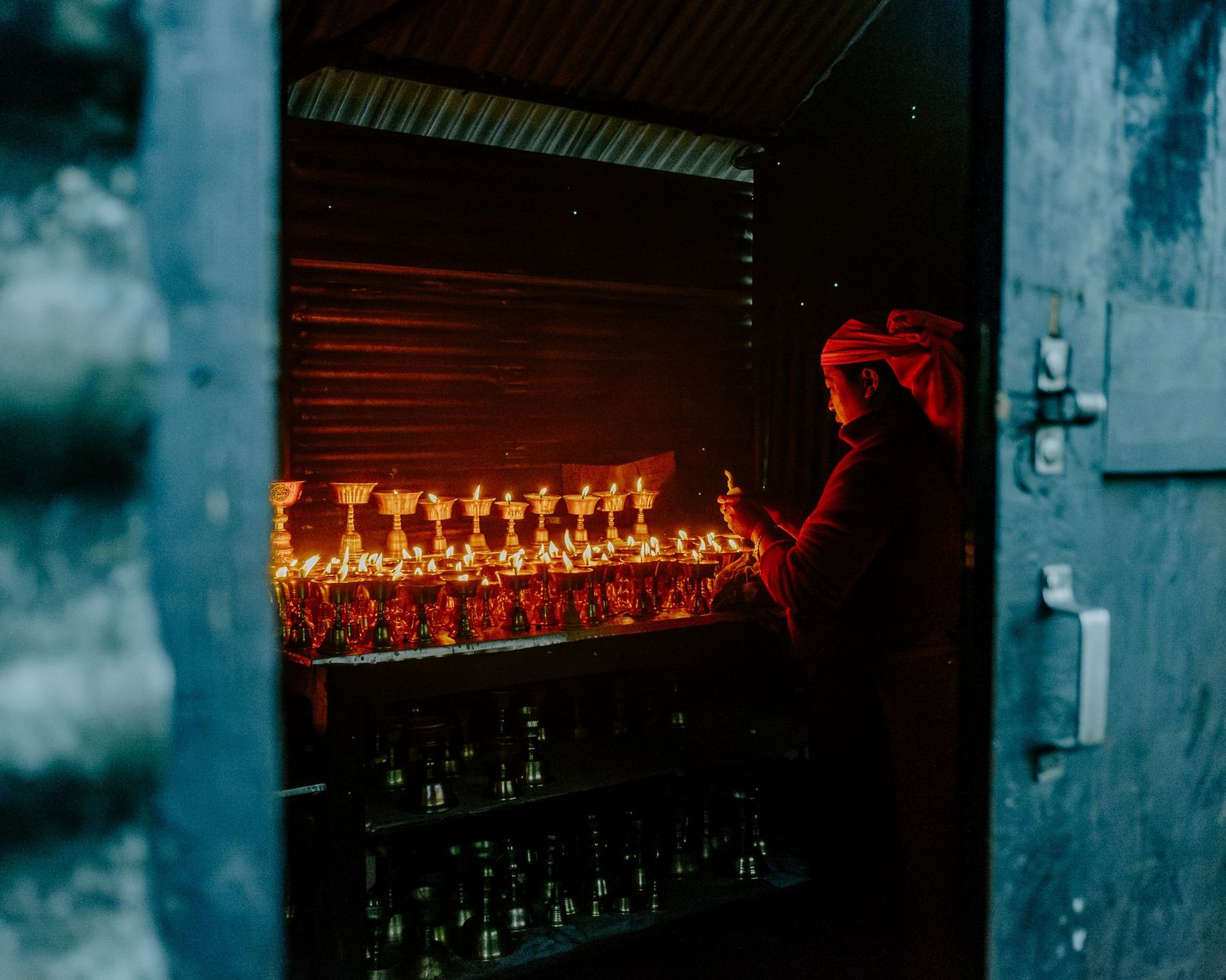 A silhouetted figure illuminated by red light tends to glowing candles in a dark, atmospheric setting.