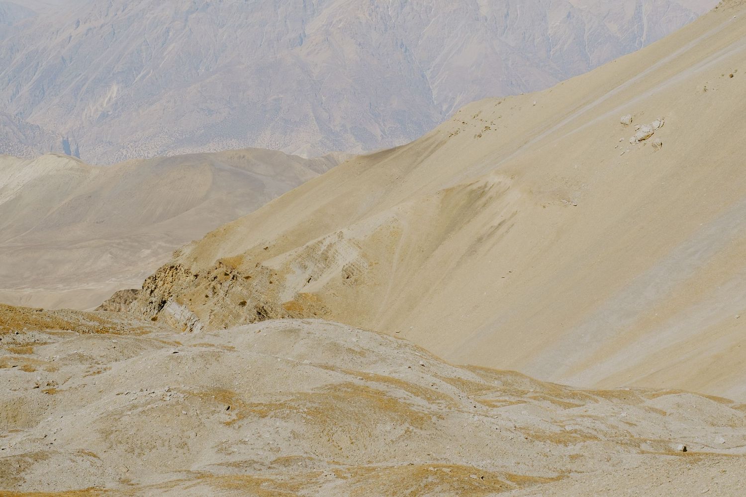 Barren desert mountainside with sandy slopes and rocky terrain in harsh sunlight.
