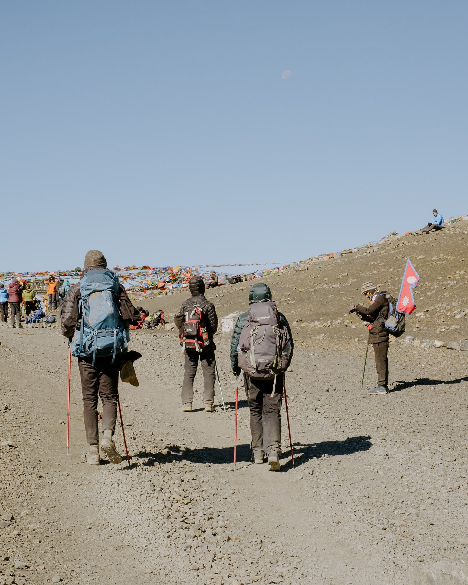 Hikers trek along a rocky mountain path carrying backpacks and hiking gear.