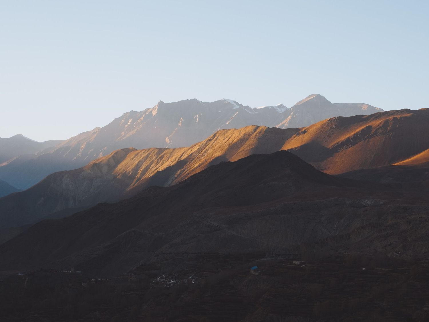 Mountain peaks cast dramatic shadows during sunset in a rugged alpine landscape.