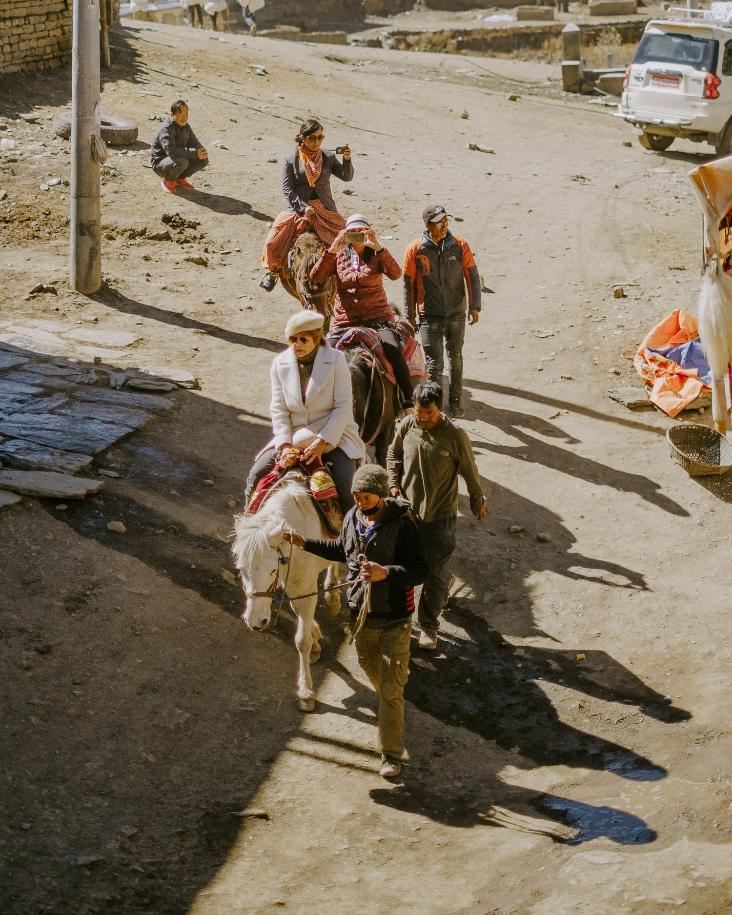 A group of tourists ride on horseback along a dusty road in a Middle Eastern setting.