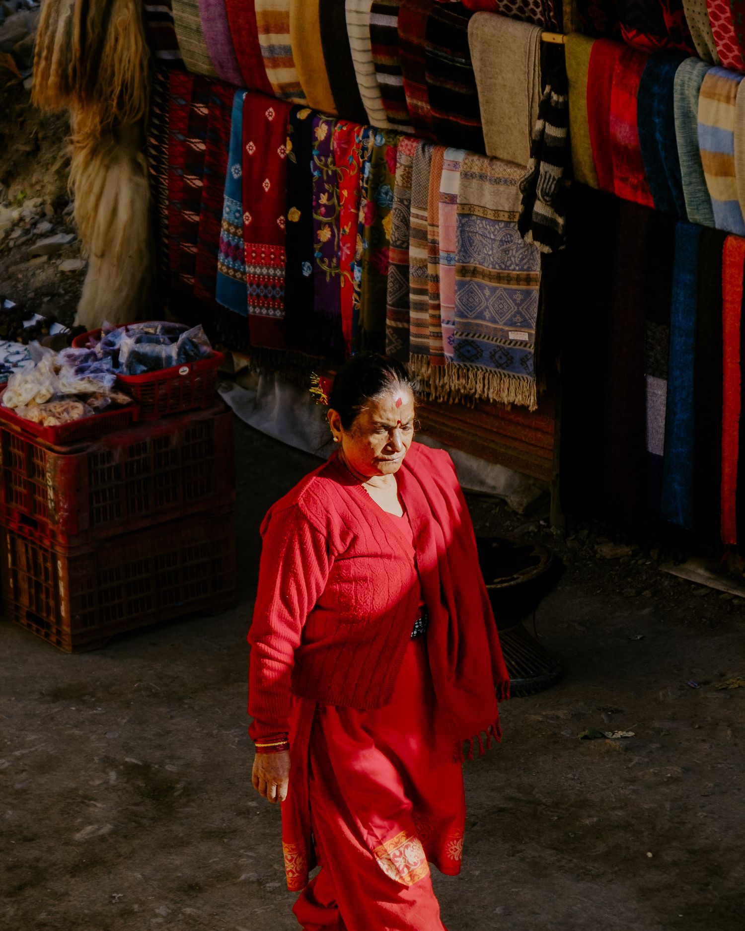 A display of colorful traditional textiles and garments hanging in a dimly lit market stall.
