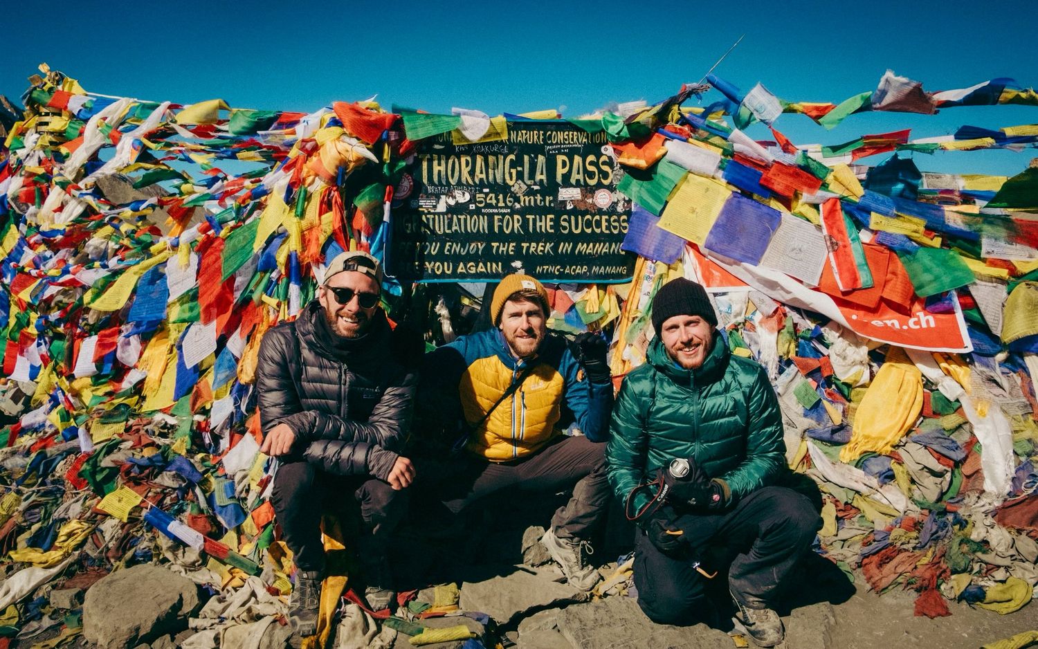 Vibrant Tibetan prayer flags stretch across a mountain vista on a clear day.