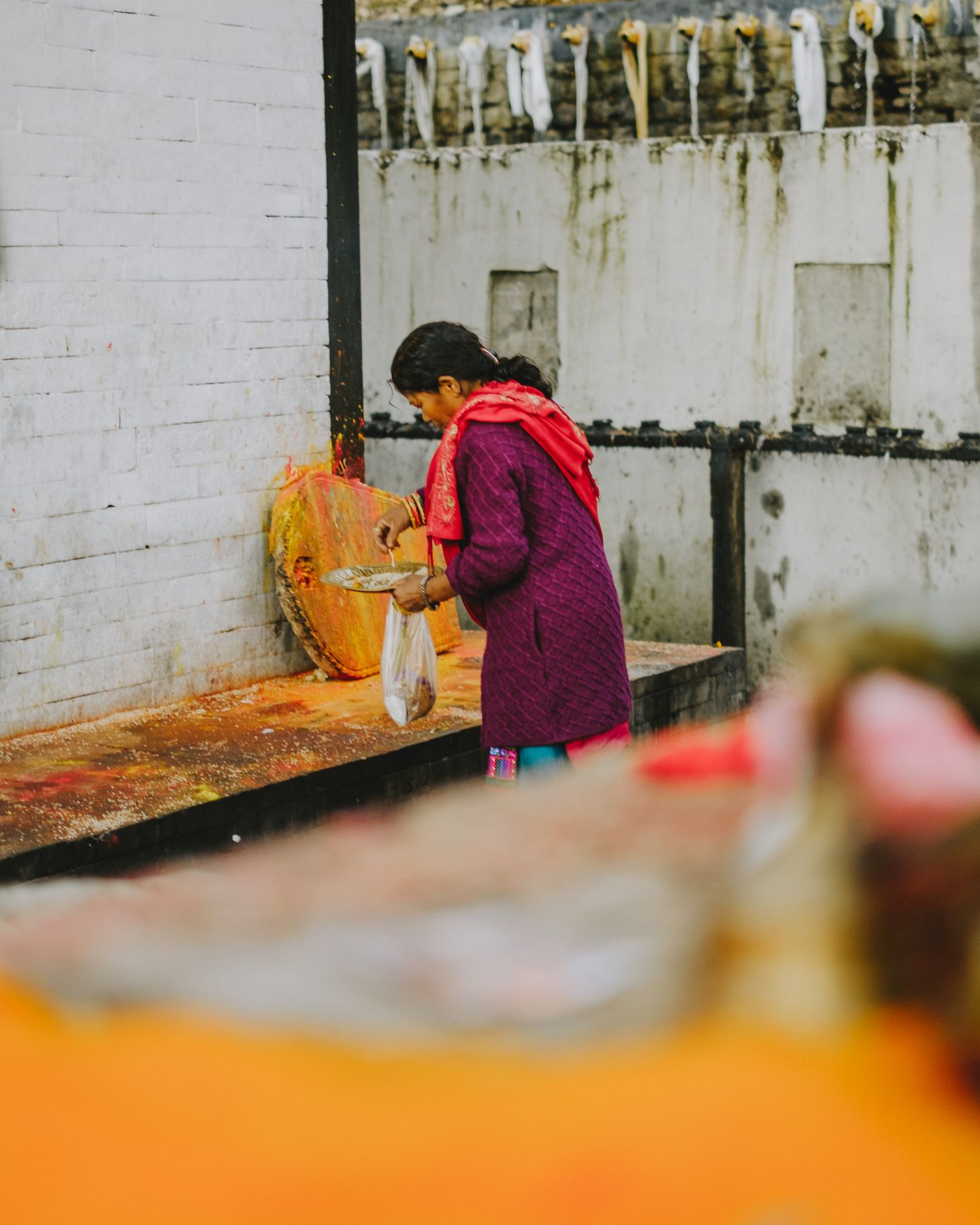 Person in colorful clothing works at a traditional pottery workshop with shelves of ceramic items in the background.