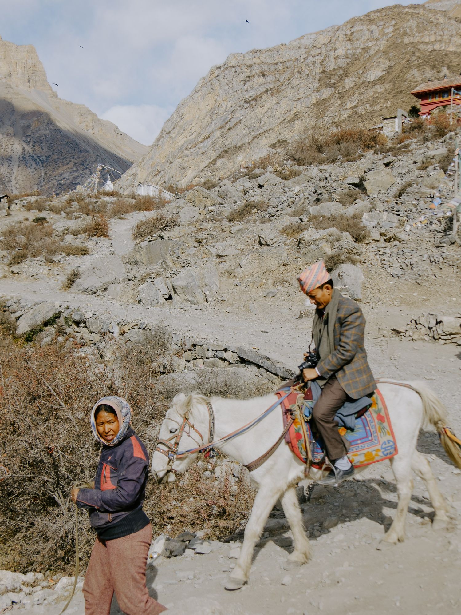 Mountain trail with loaded pack animals traversing a rocky terrain surrounded by steep cliffs.