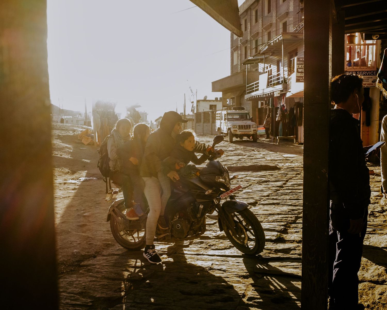 Silhouettes of motorcycles and people are backlit by golden sunlight on a cobblestone street.
