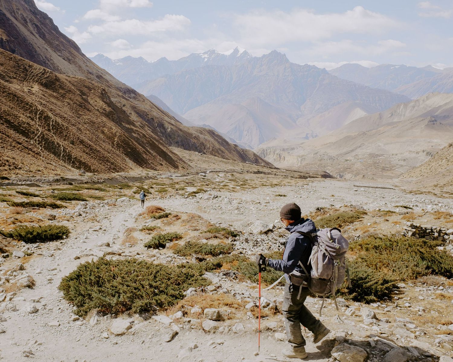 Hikers with backpacks walking along a remote mountain trail surrounded by rugged peaks.