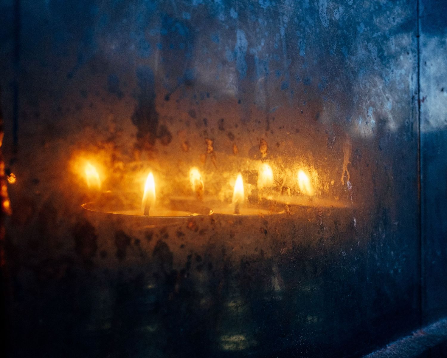 Row of glowing candles creating warm illumination against a dark textured background.