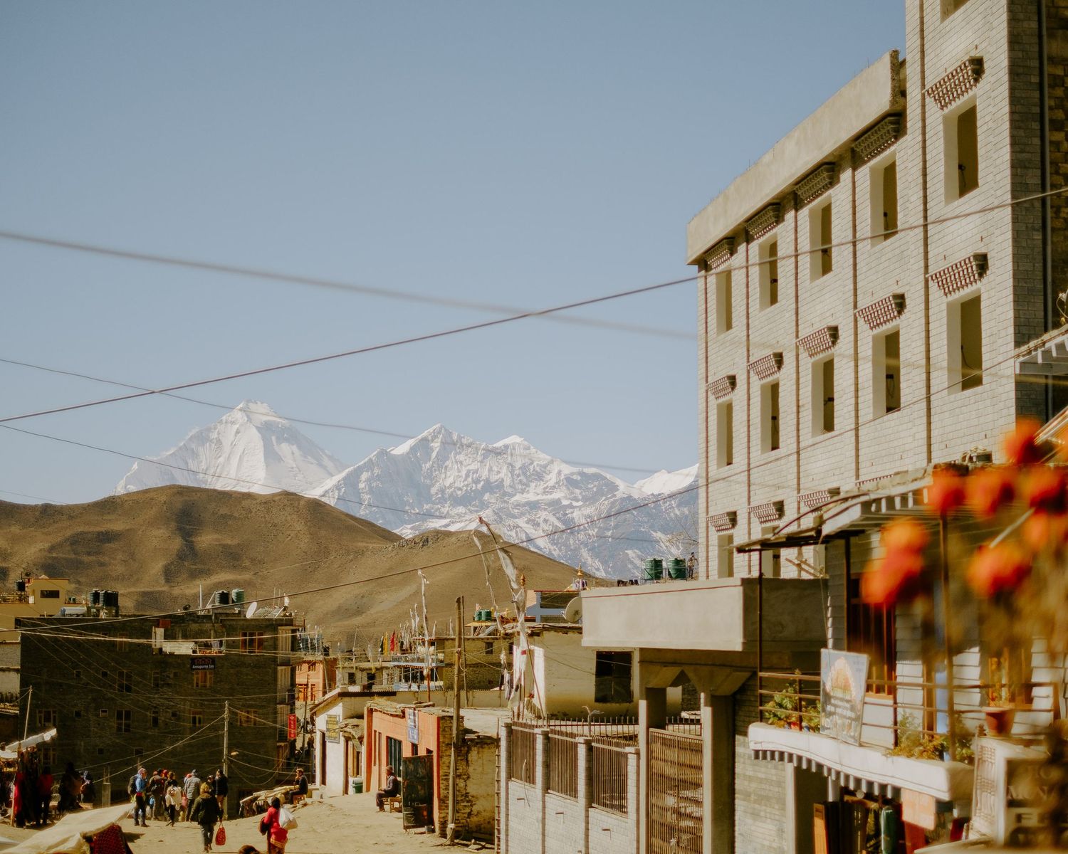 Snow-capped mountains rise behind a row of modern buildings along a street in a Tibetan town.