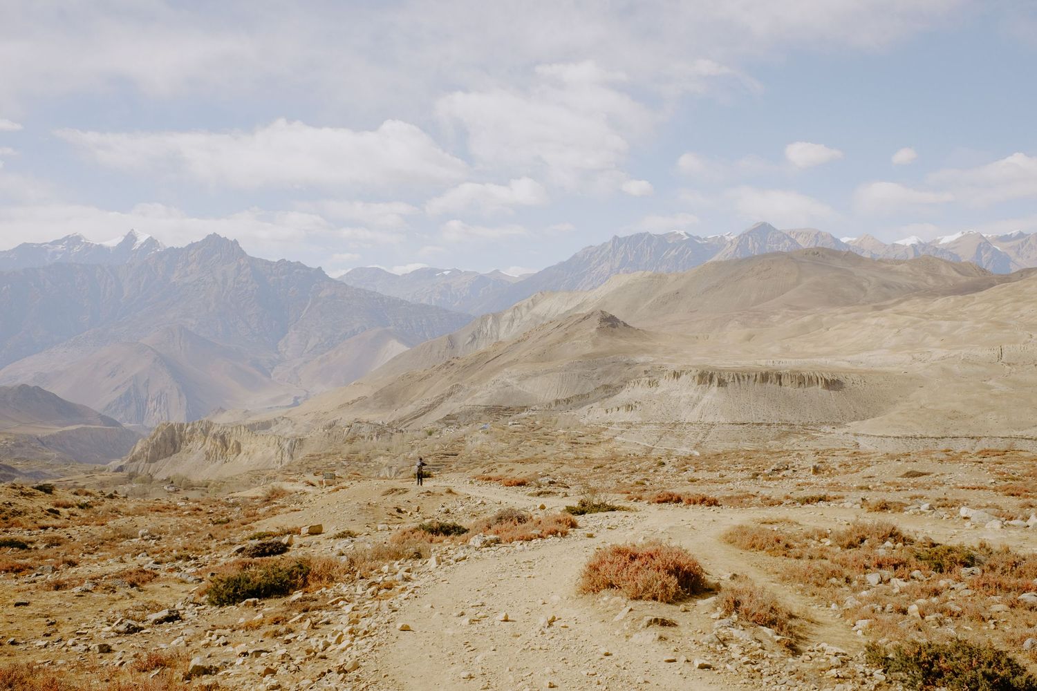 Wide mountain landscape with barren slopes and distant peaks under a cloudy sky.