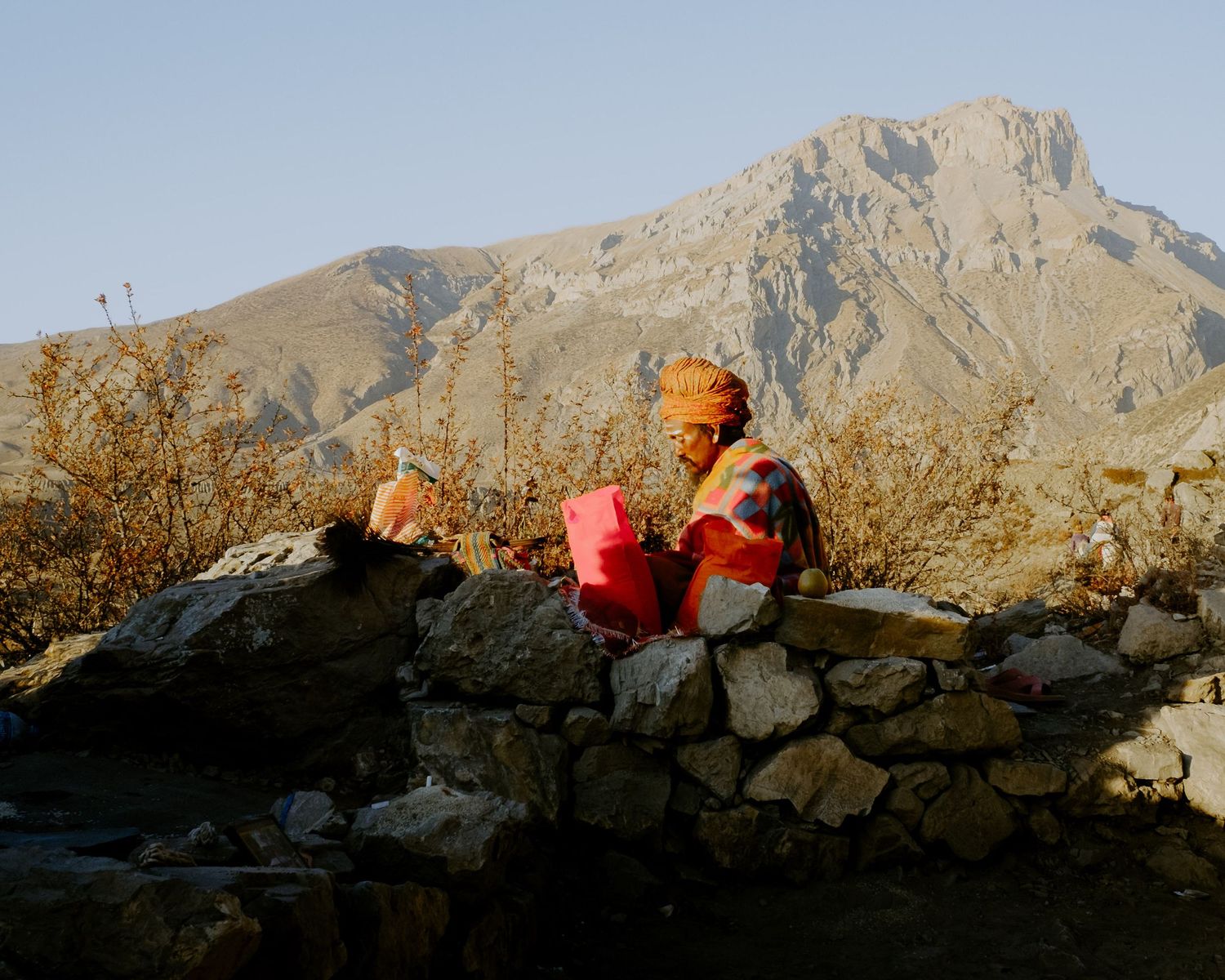 People relax against stone wall with dramatic mountain peak rising in background during golden hour.
