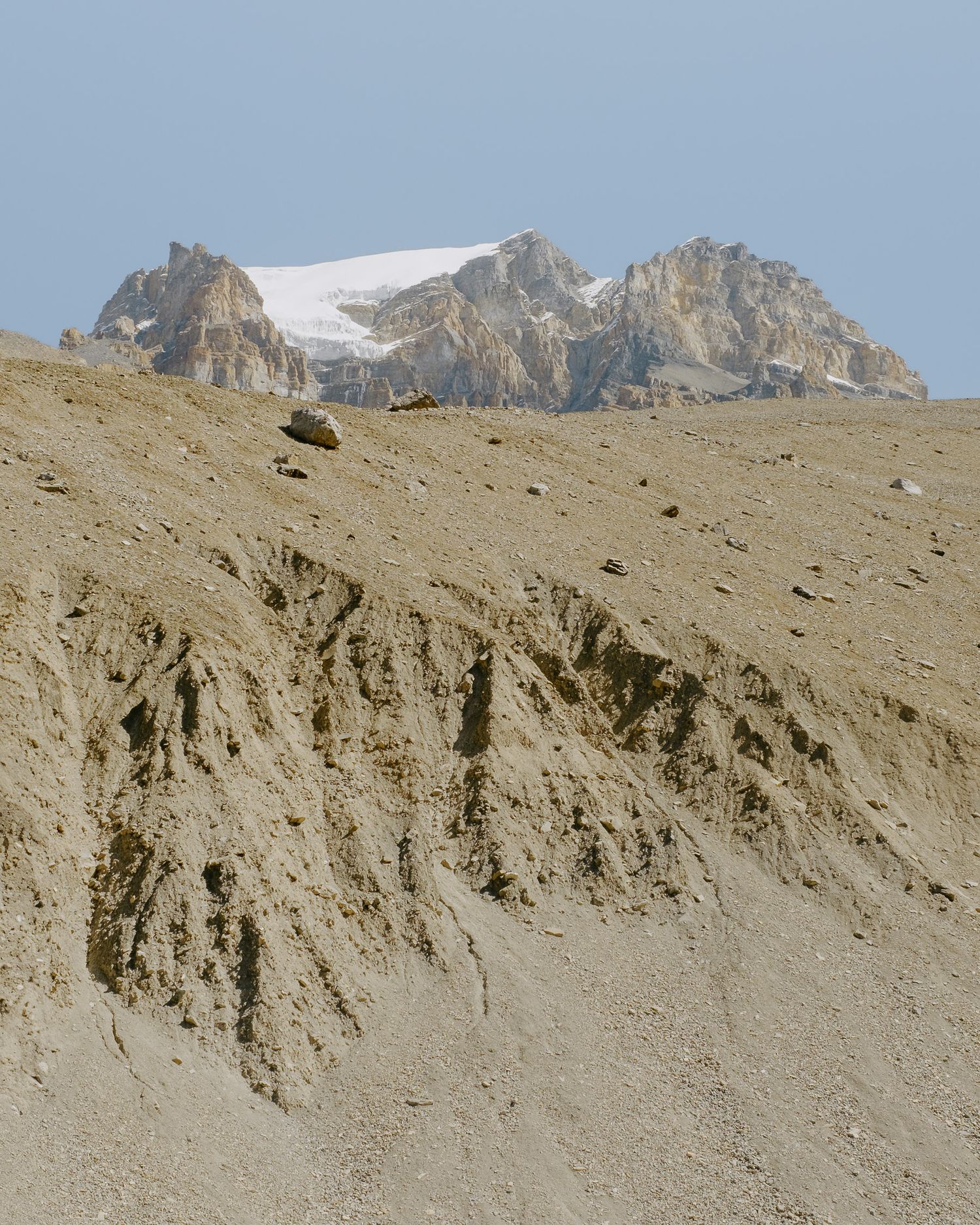 Snow-covered mountain peak rising above barren slopes against a pale blue sky.