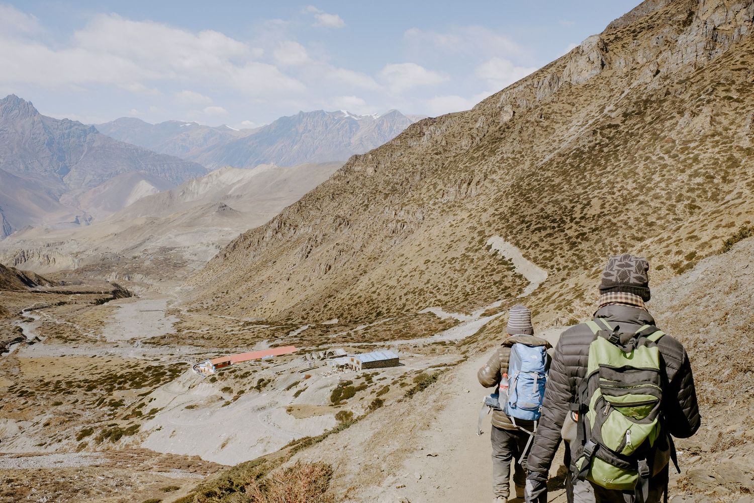 Backpackers navigate a winding mountain path through rugged high-altitude terrain.