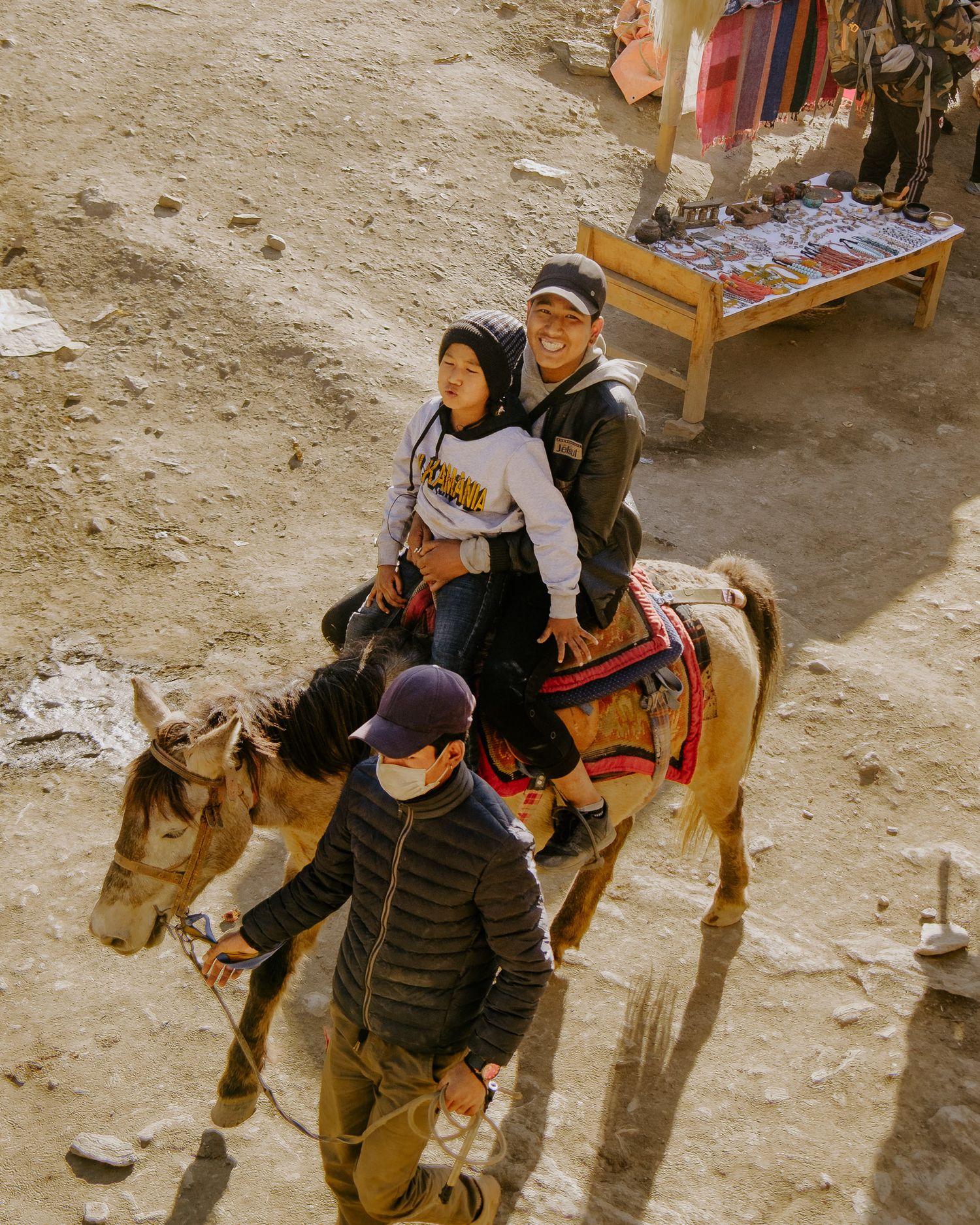 Travelers with backpacks and winter gear walk along a dusty mountain path.