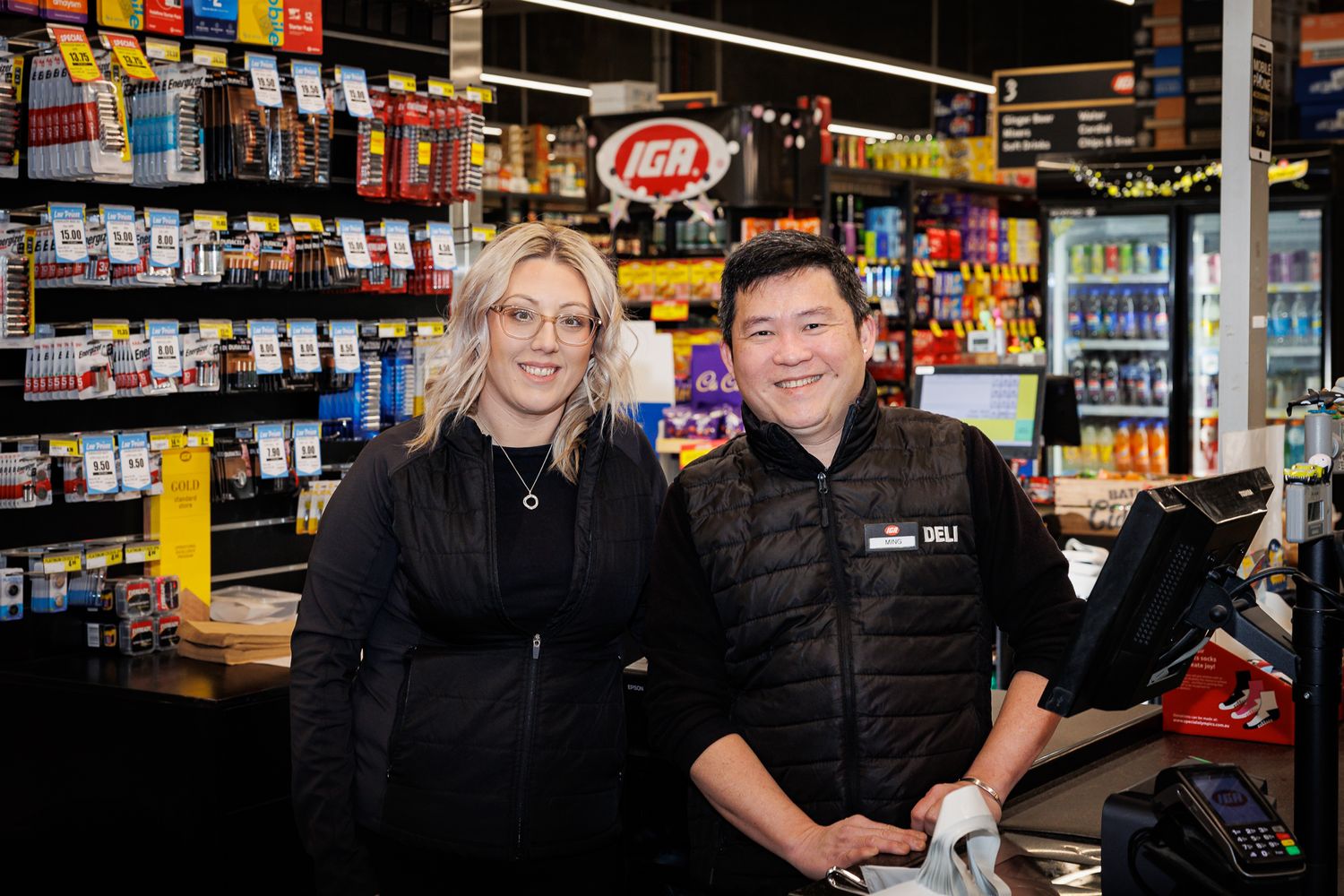 Staff members inside an IGA store with shelves of groceries in background.
