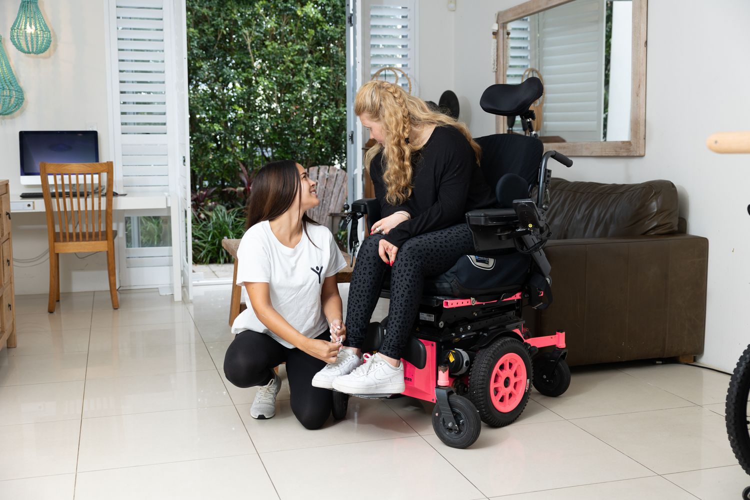 Physical therapist assisting patient with powered wheelchair settings in a bright indoor setting.