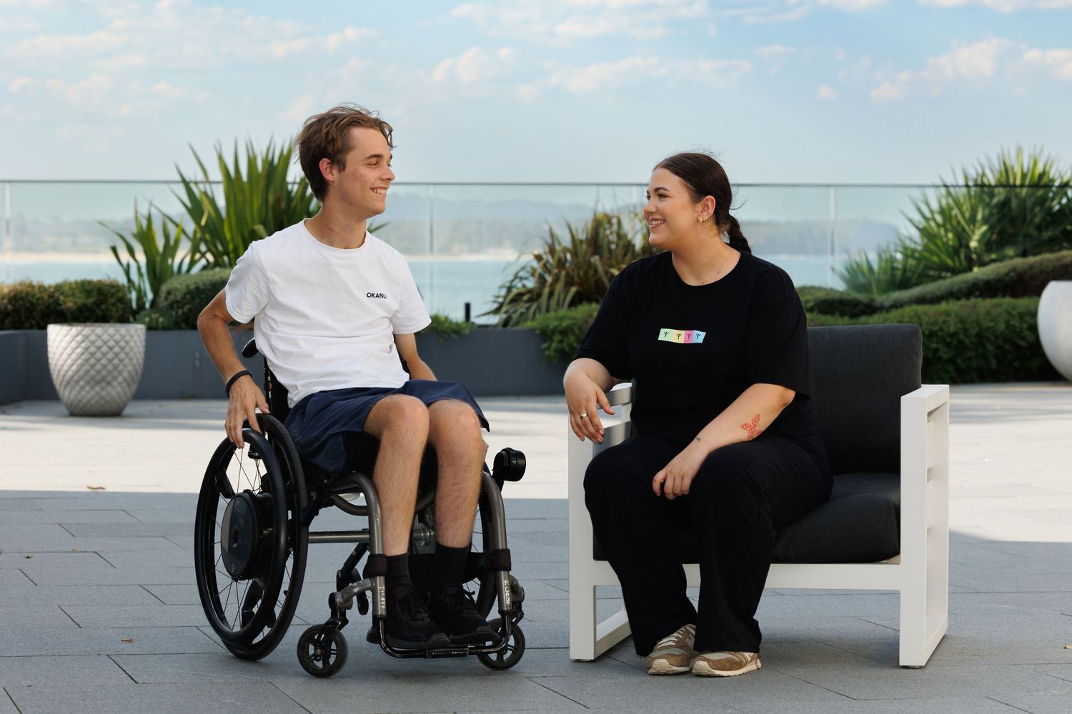 Two people having a friendly conversation on an outdoor patio with ocean views.