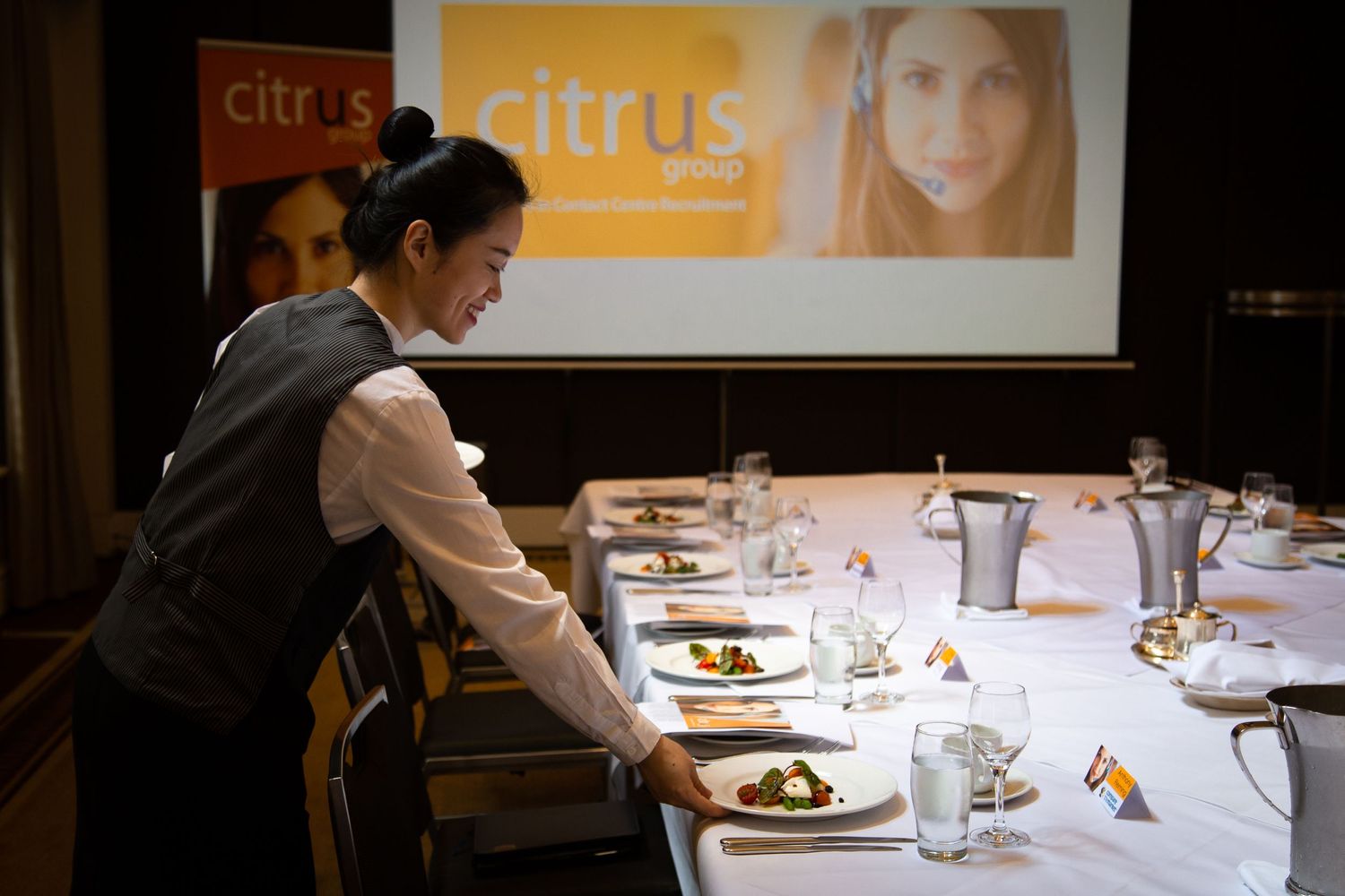Sydney Event Photography - A server sets plates at an elegant dining event with Citrus branding displayed.