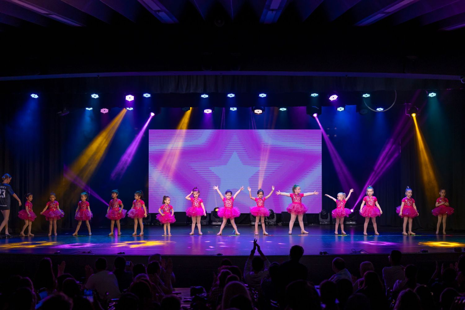 Dance performers on stage with colorful lighting and costumes in a theatrical production.