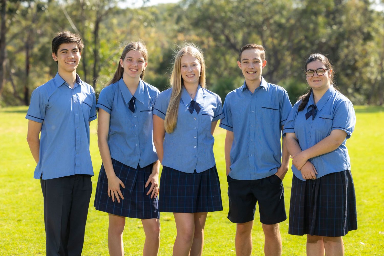 Group of students in matching blue polo uniforms standing together on sunny grass field.