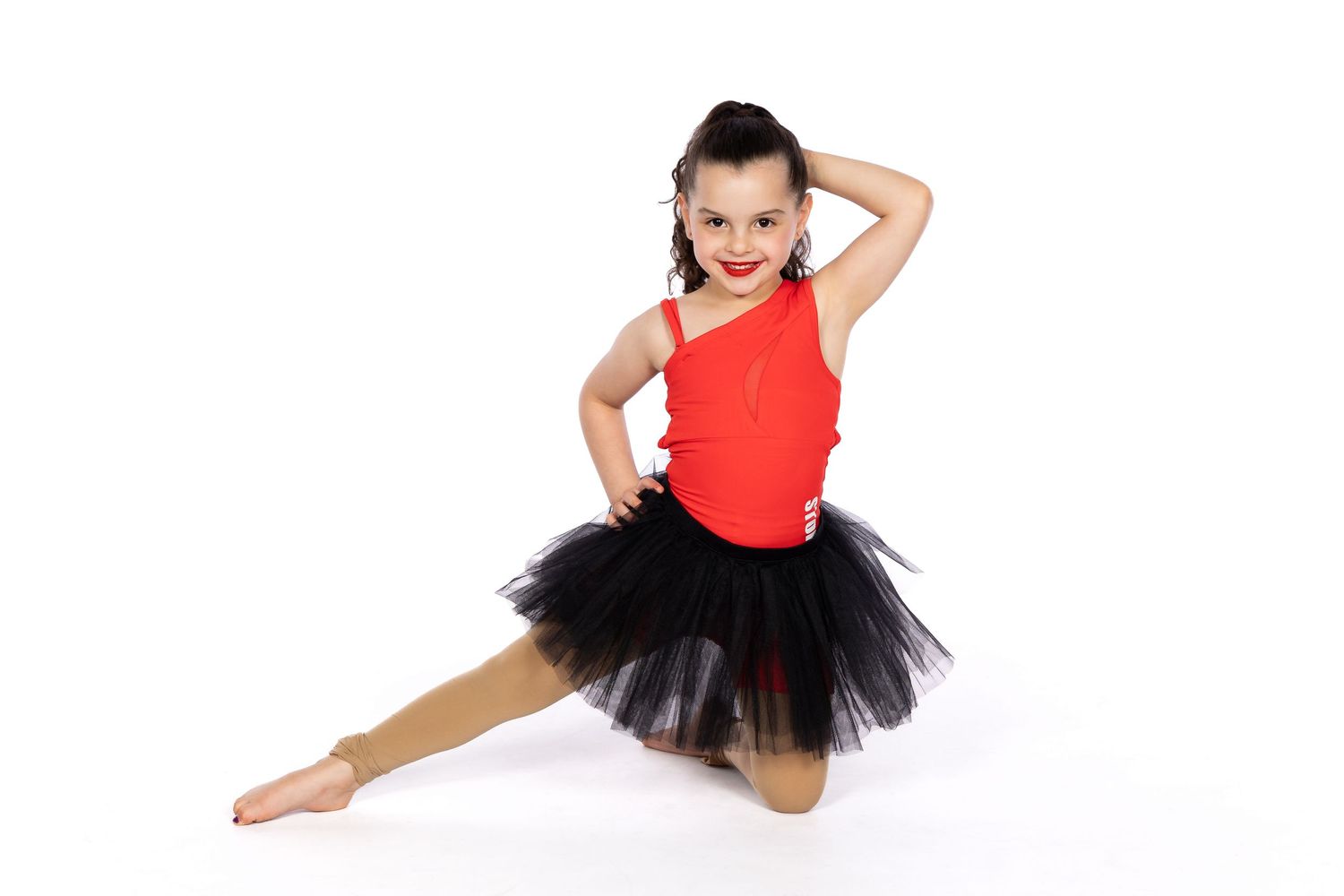 A dancer in a red top and black tutu performs a graceful pose on the floor.