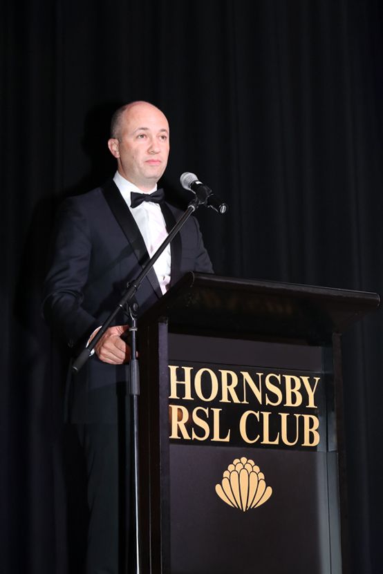 Sydney Event Photography - A speaker in a tuxedo stands at a podium at the Hornsby RSL Club.