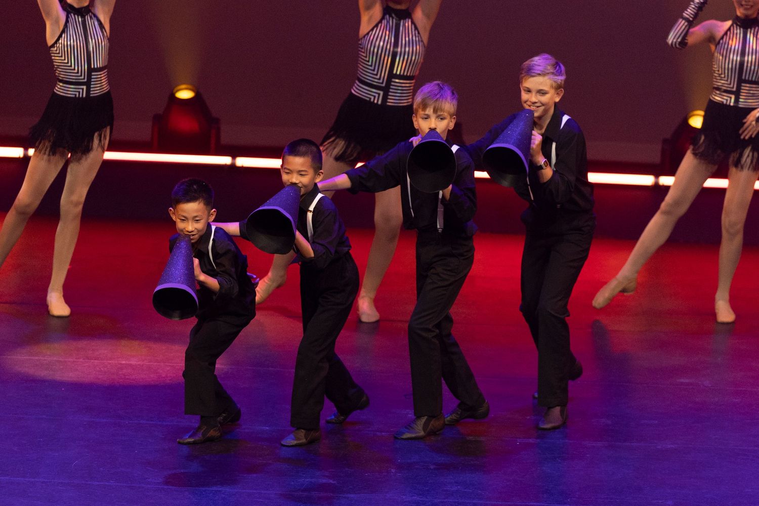 Group of young dancers performing choreographed routine in formal attire on purple-lit stage.
