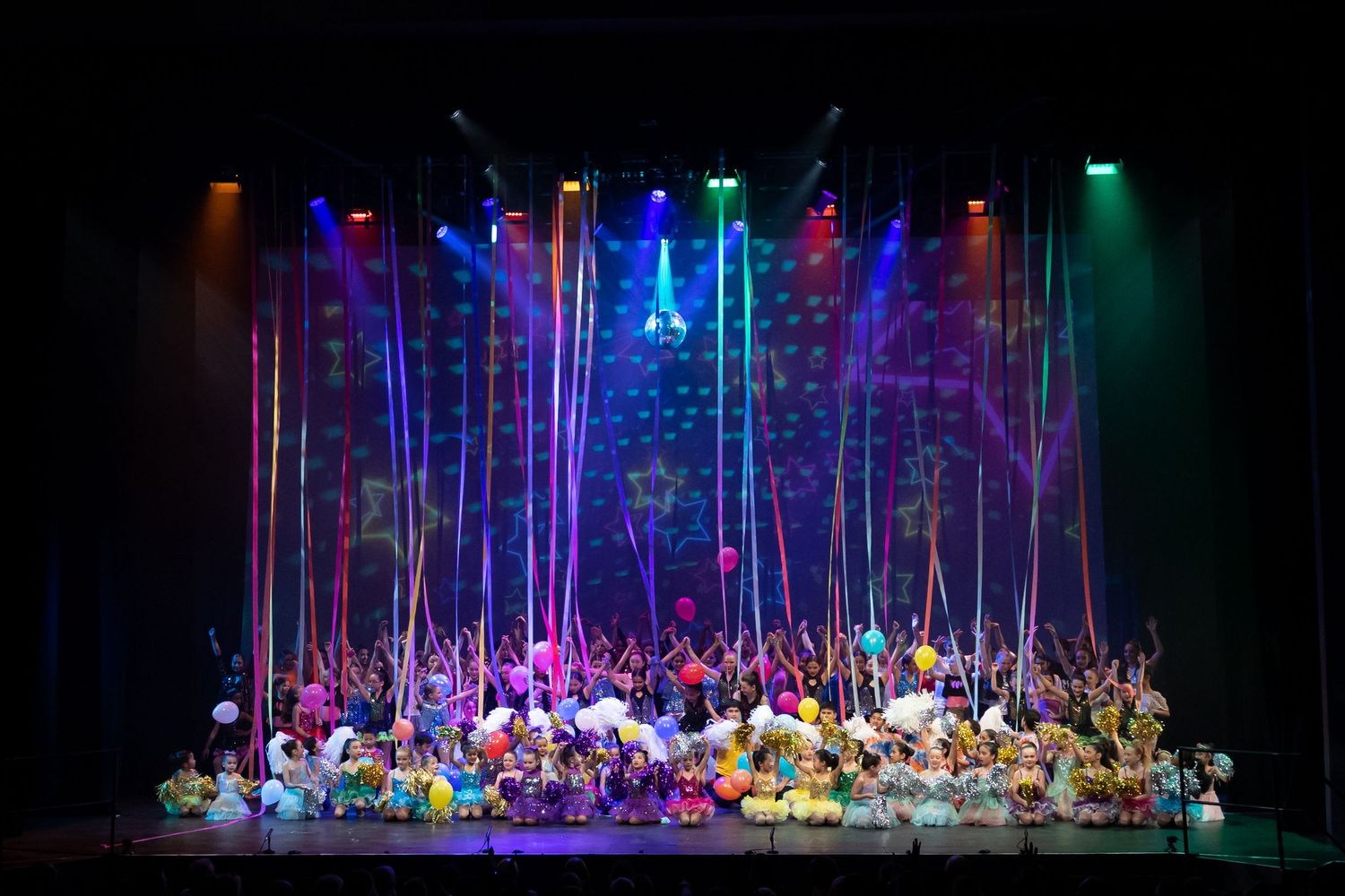 Colorful stage production with elaborate forest-themed set design and dramatic lighting effects.