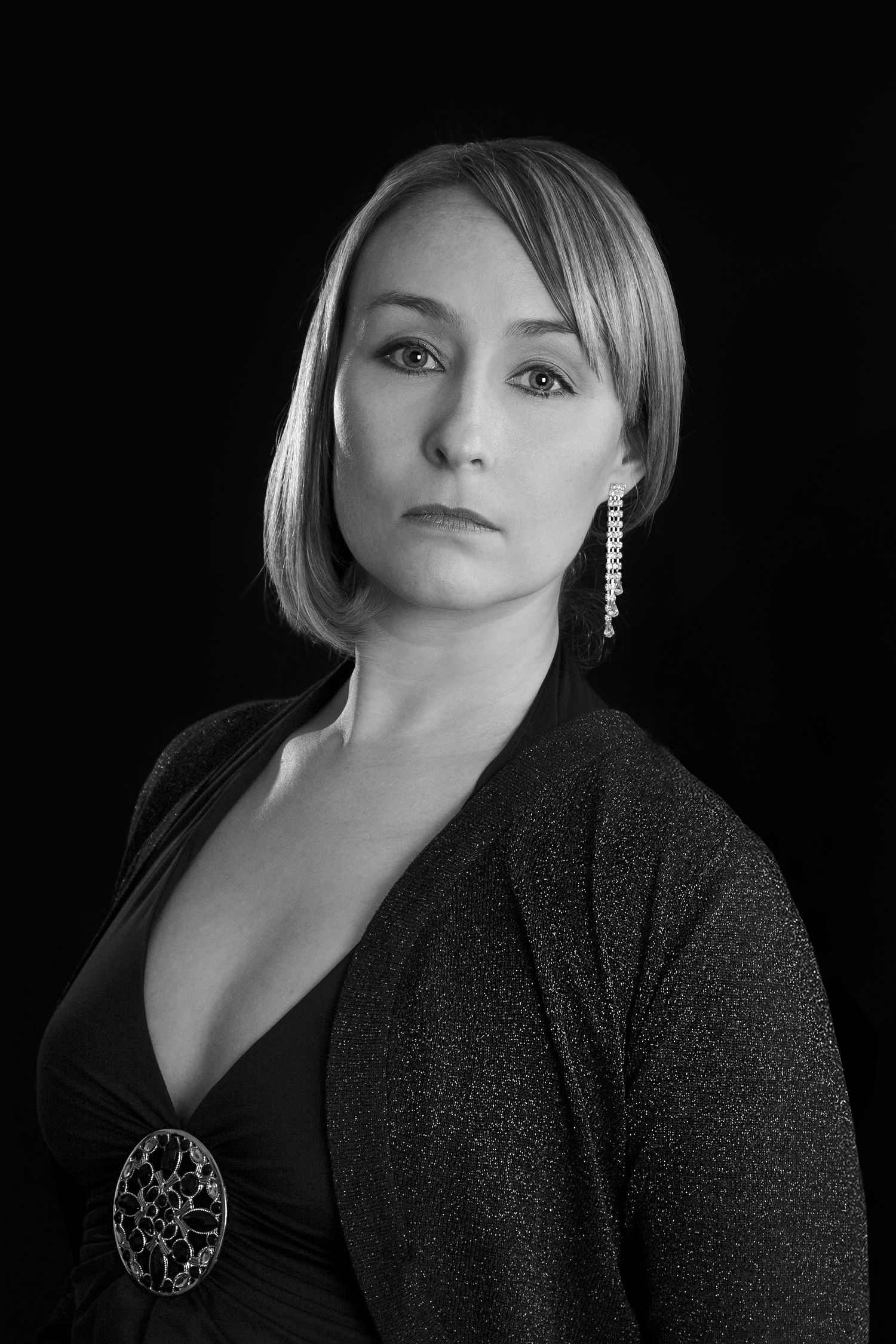 Dramatic black and white portrait of a person with dangling earrings and ornate broach.