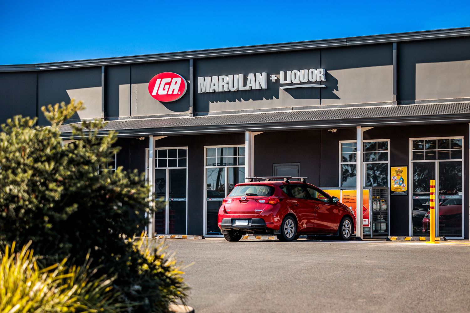 IGA Marulan store exterior with red car parked in front.