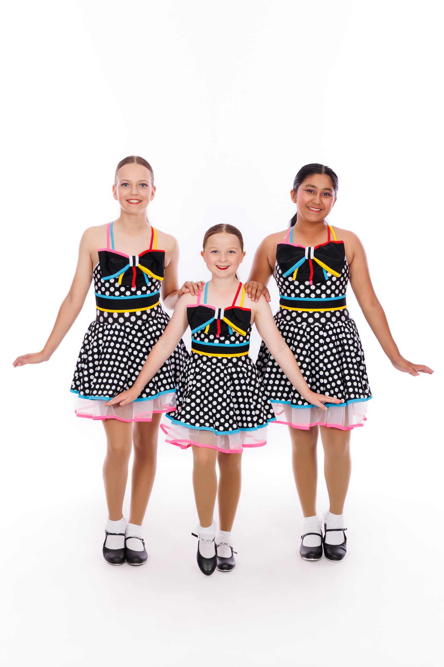 Three dancers in matching polka dot dresses with colorful trim posing together.