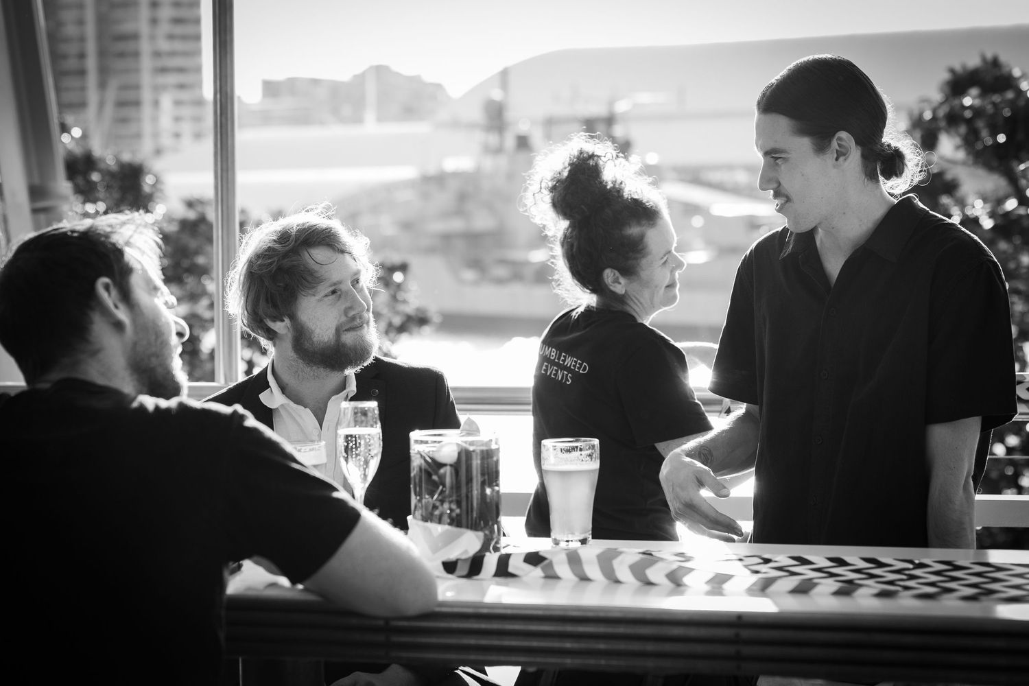People gather at a bar counter enjoying drinks and socializing in a dimly lit establishment.