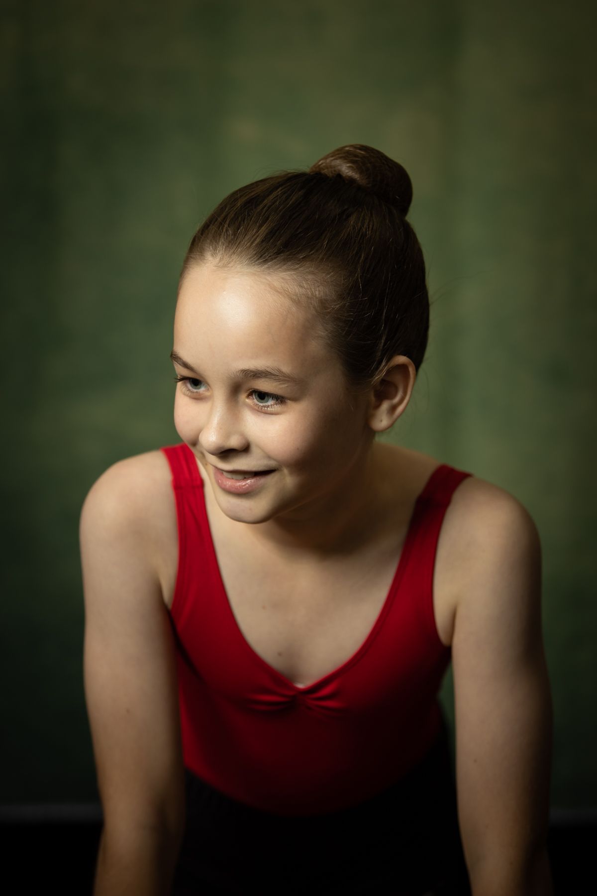 Dancer in red leotard poses against dark green background.