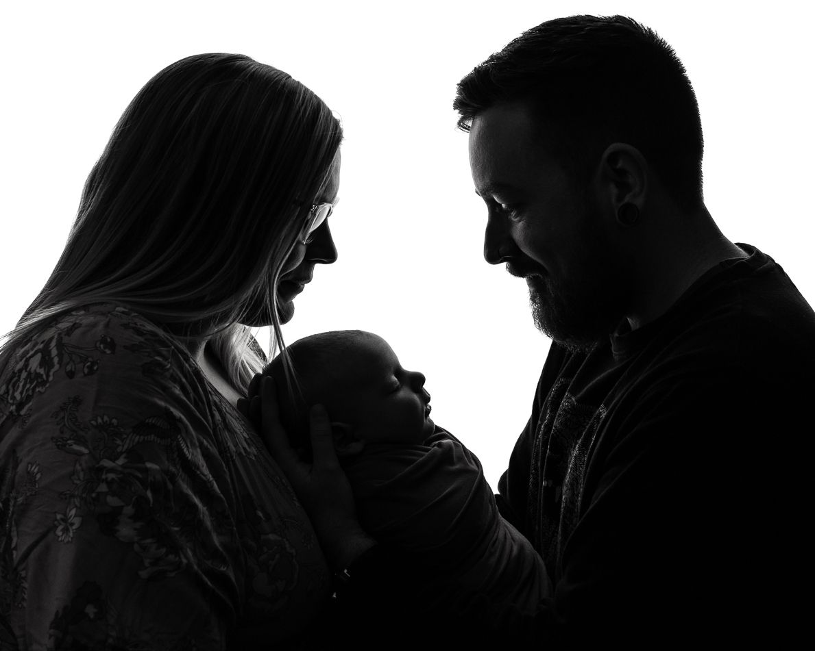 Black and white silhouette of adults looking down at a baby together in a tender family moment.