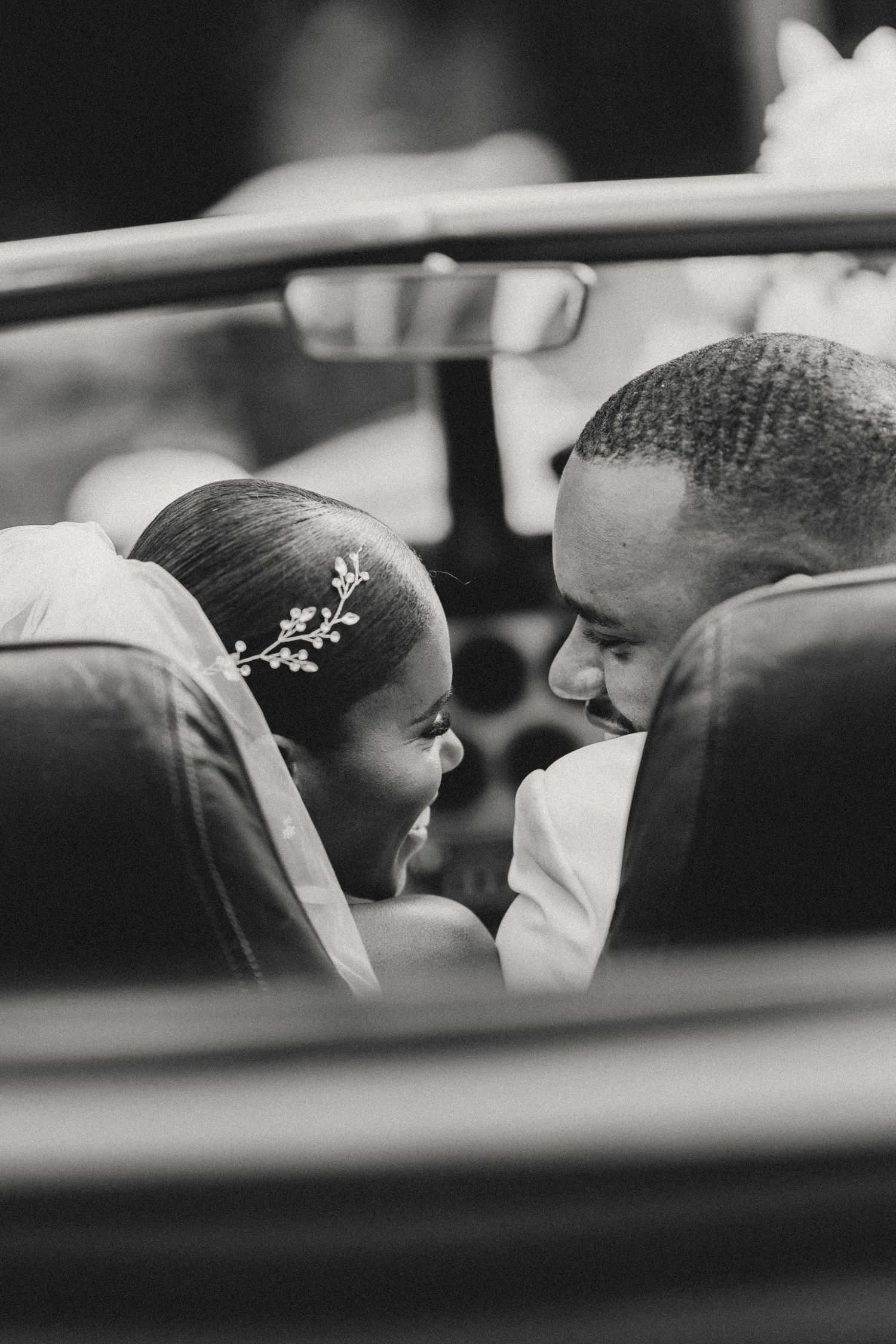 A black and white photo of a couple sharing an intimate moment in a car, captured through the window frame.