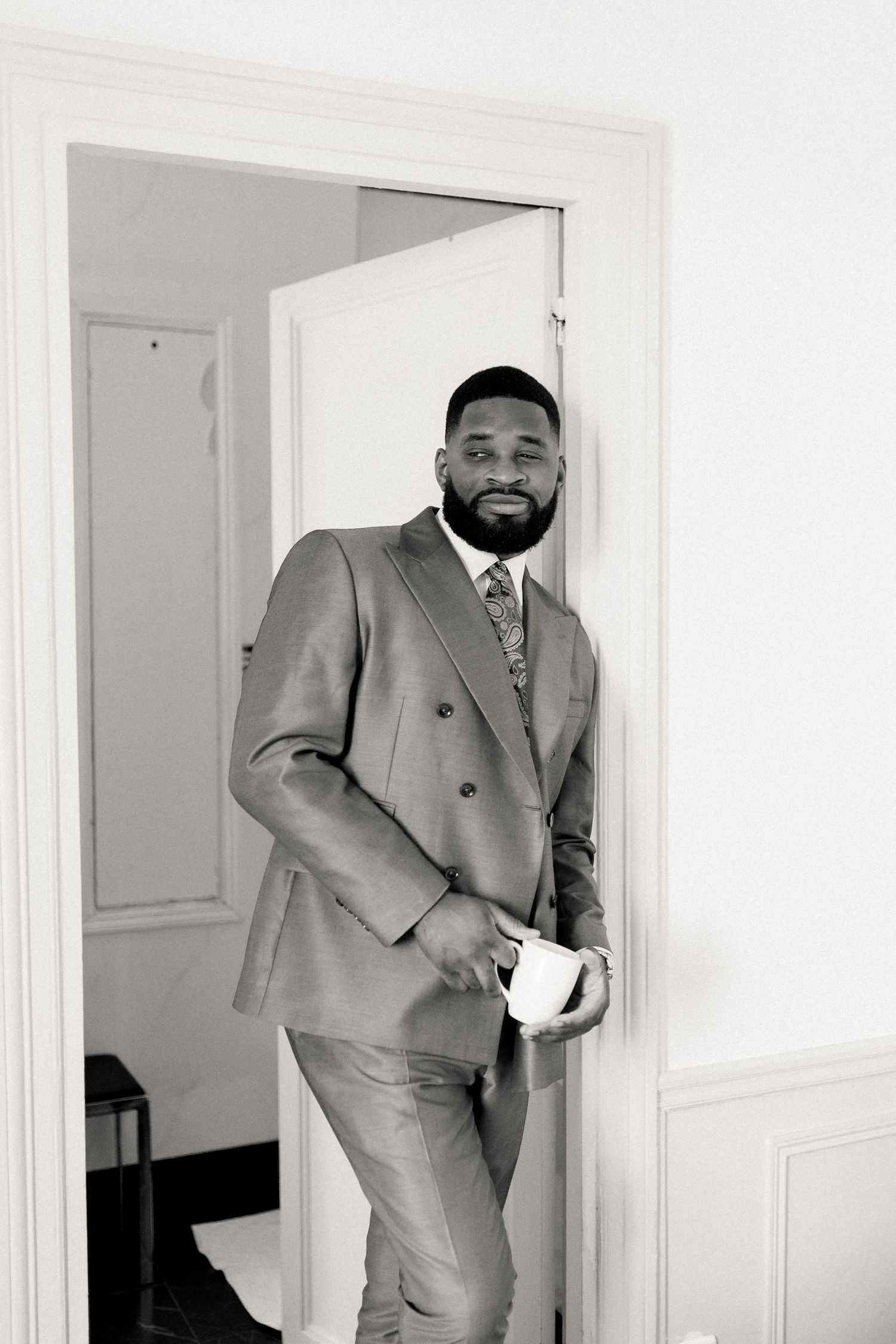 Sequence of someone in a grey suit playfully peeking around a white doorway.