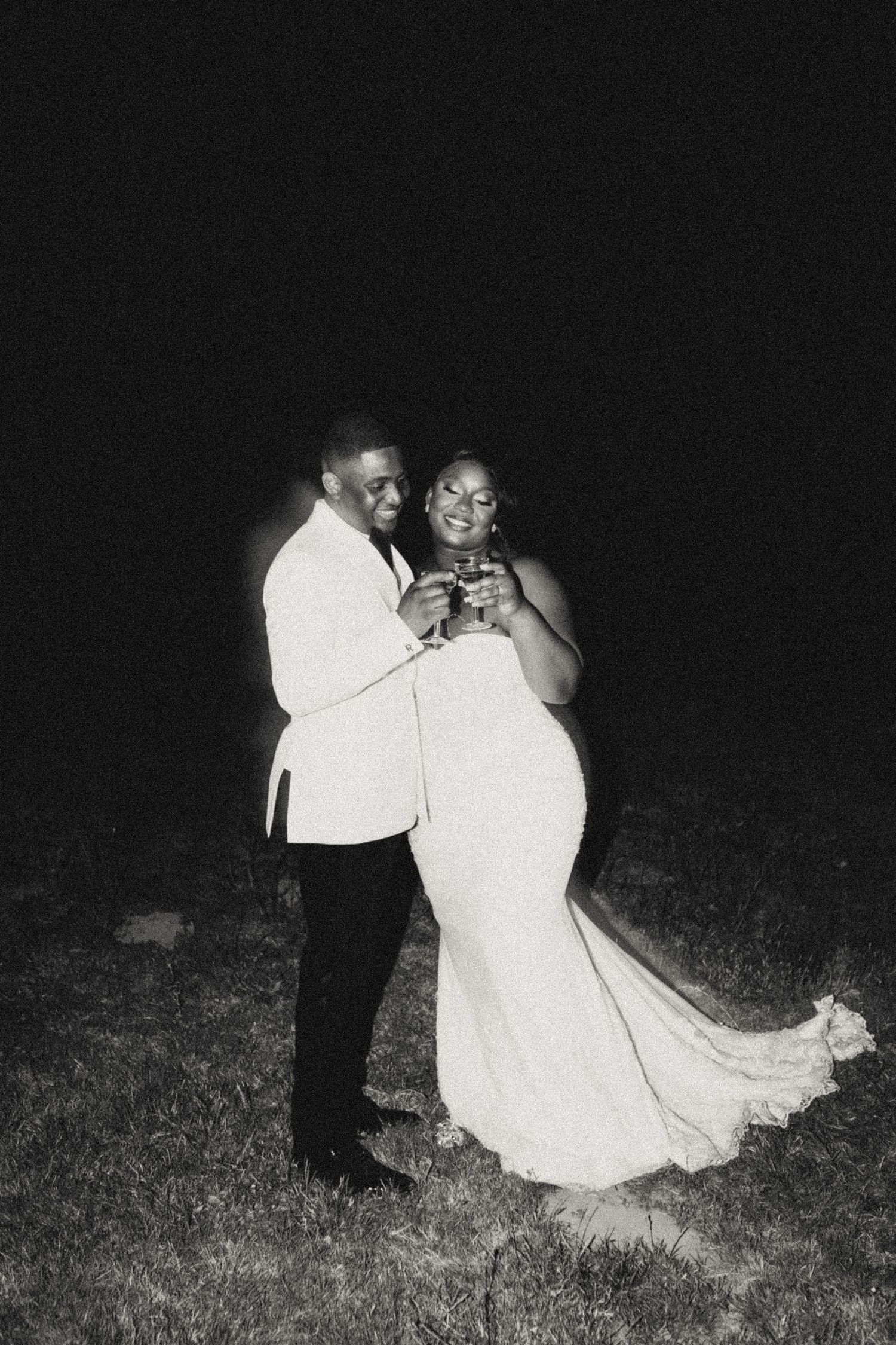 Couple in formal attire dancing together on grass at night.