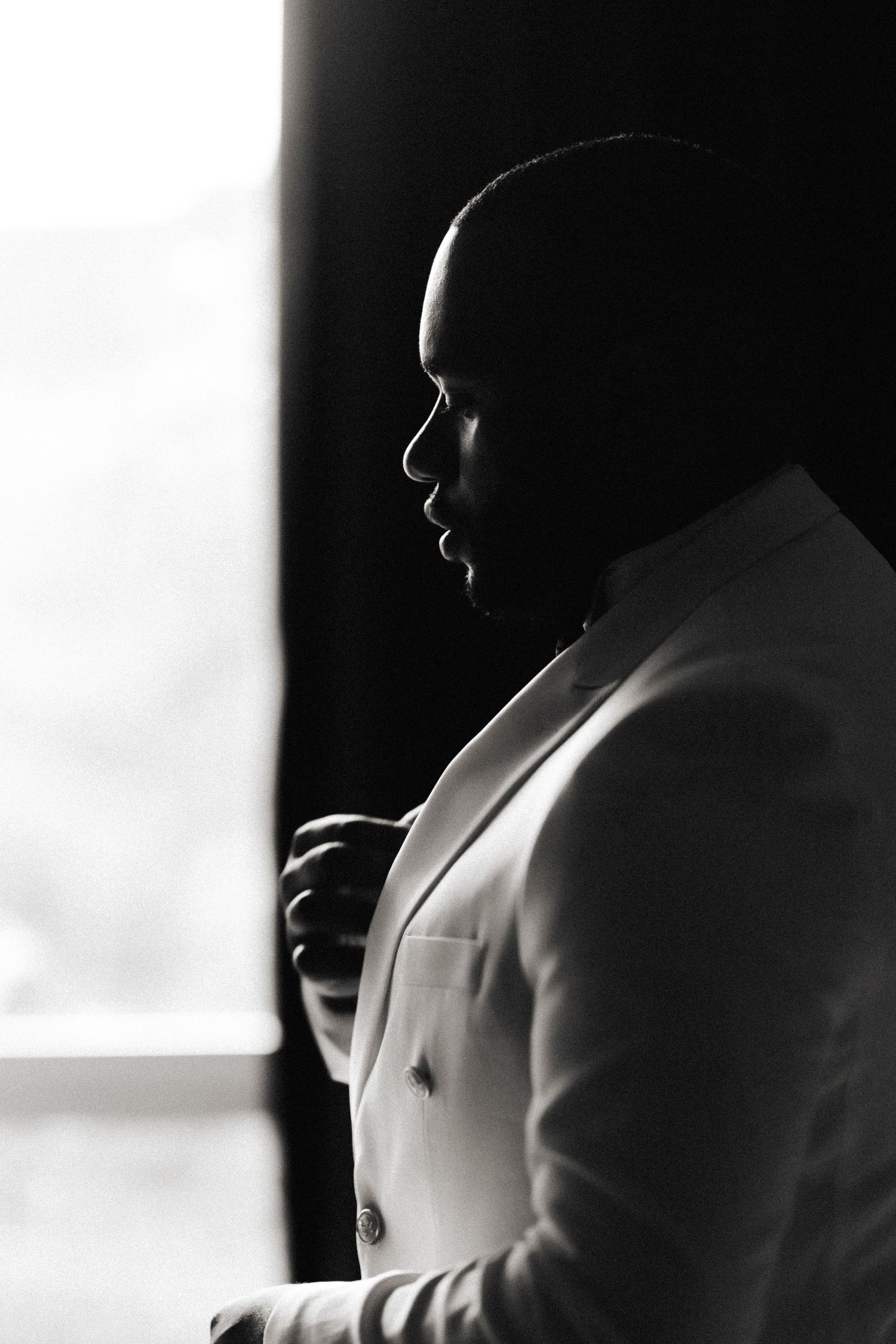 Dramatic black and white silhouette portrait showing a person in profile wearing a white jacket against dark background.