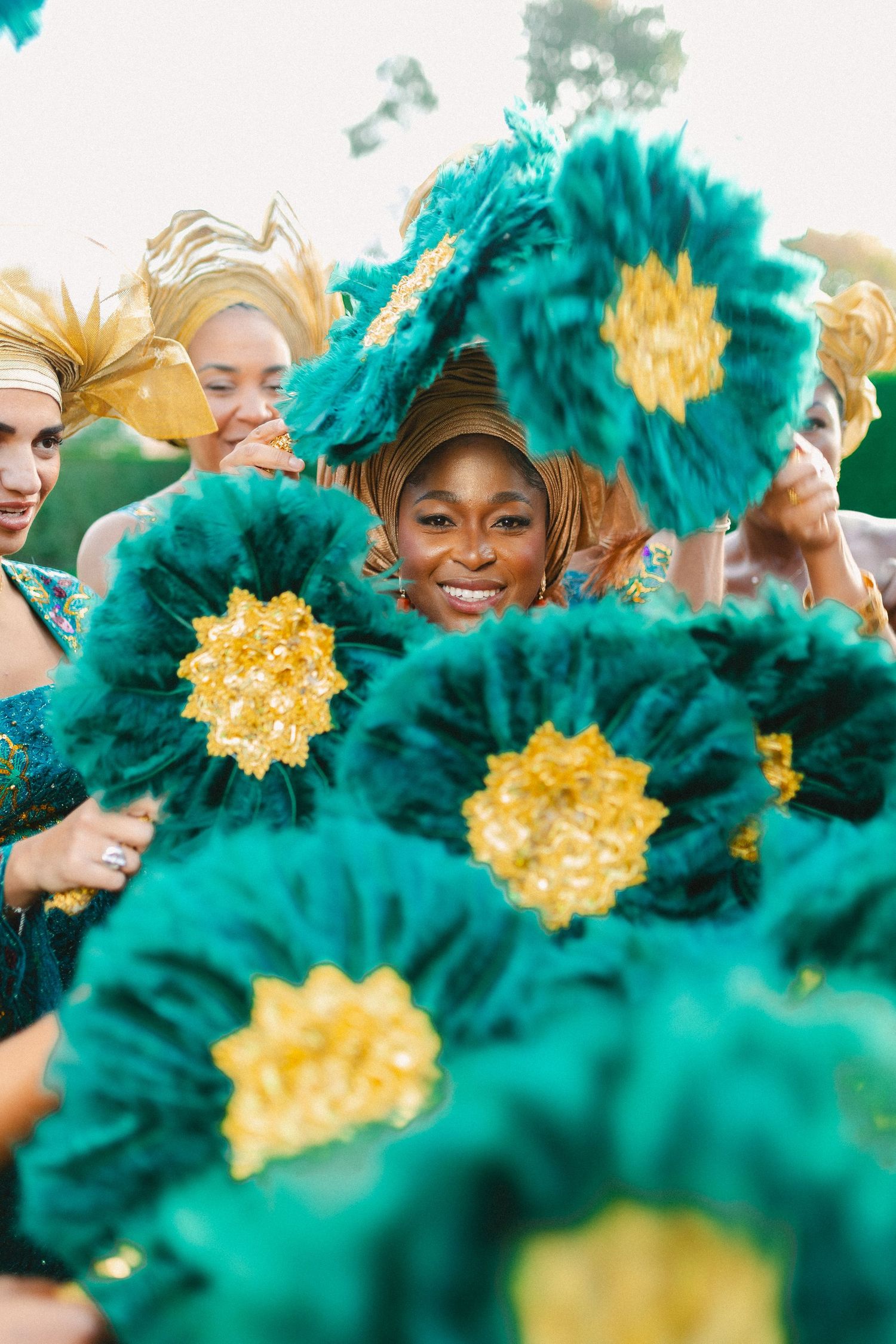 Cheerful group holding large teal and gold decorative flowers during an outdoor celebration or performance.