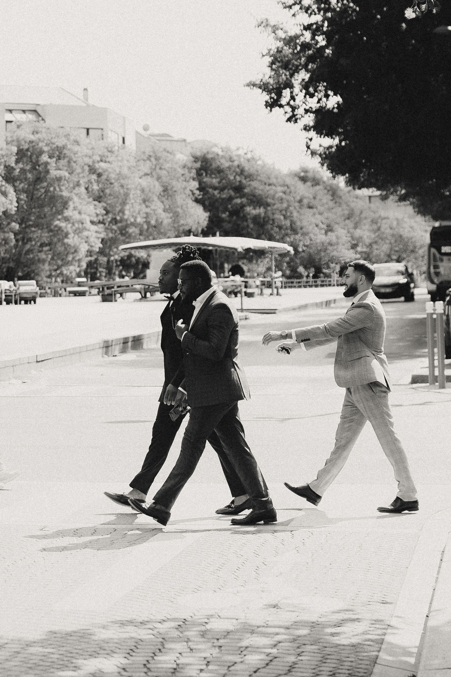 Three people in suits walking across a street in a vintage black and white photograph.