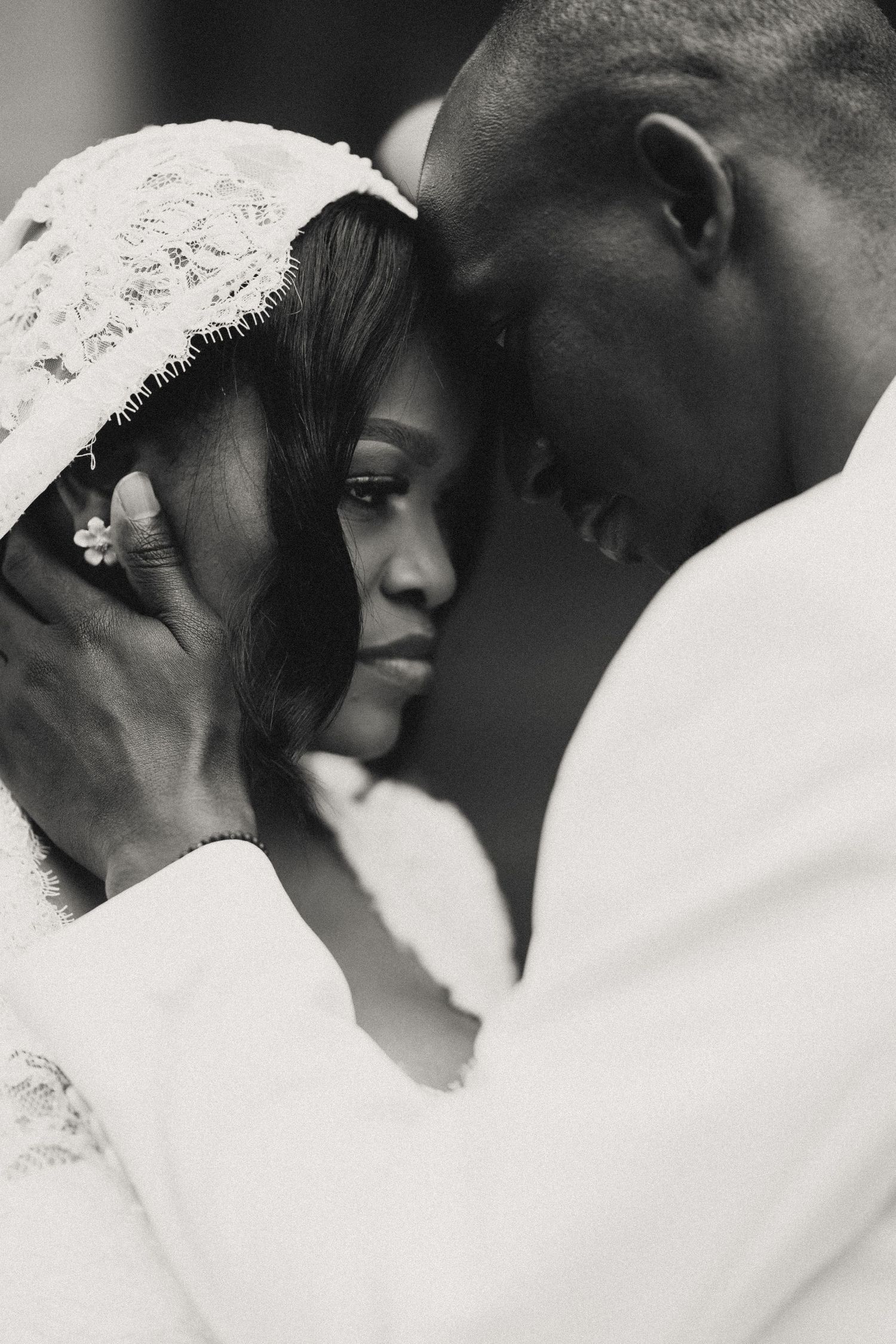 Intimate black and white portrait showing tender moment between couple in white attire.