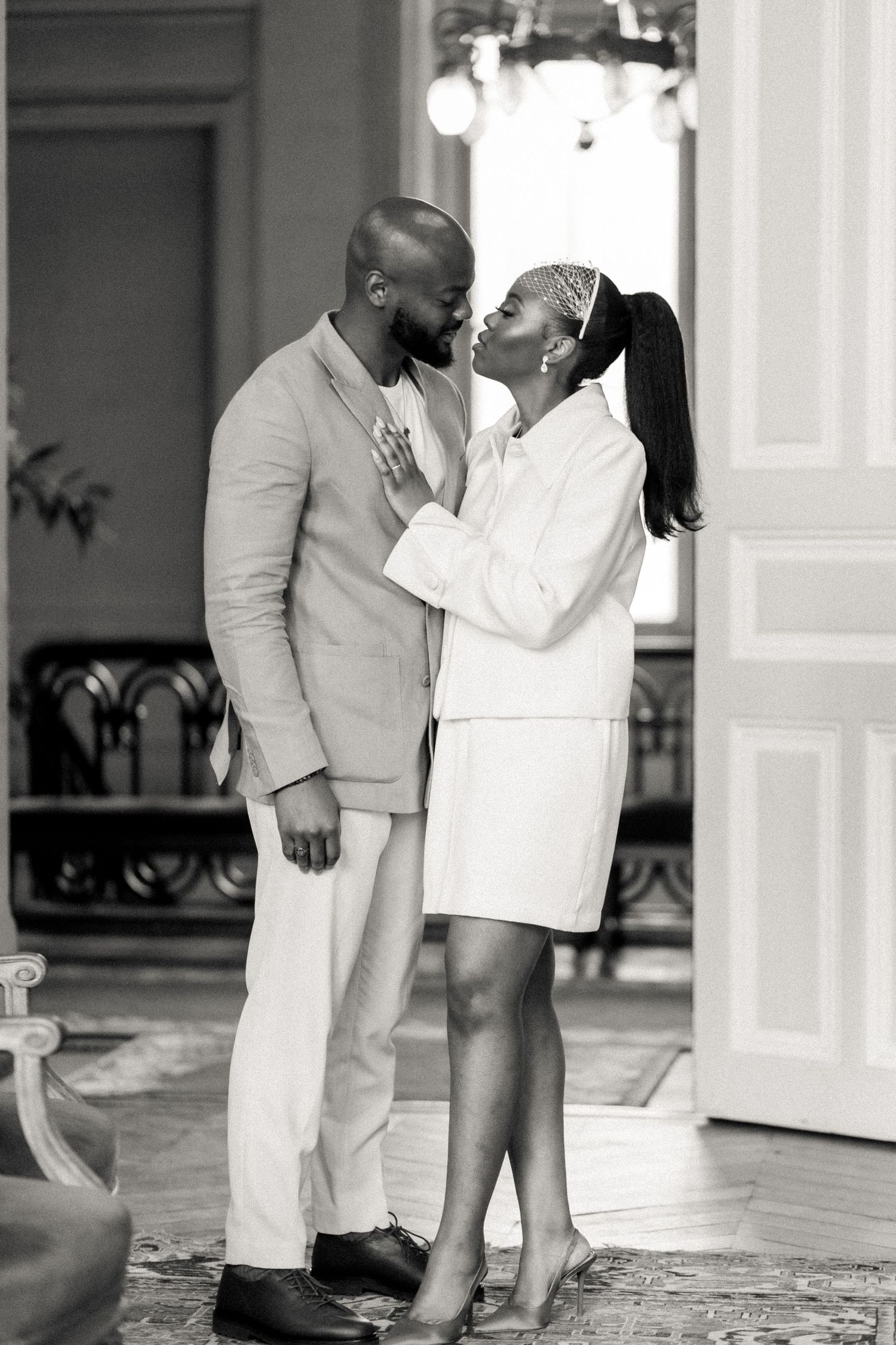 Couple in white outfits sharing a tender moment in an elegant interior setting.