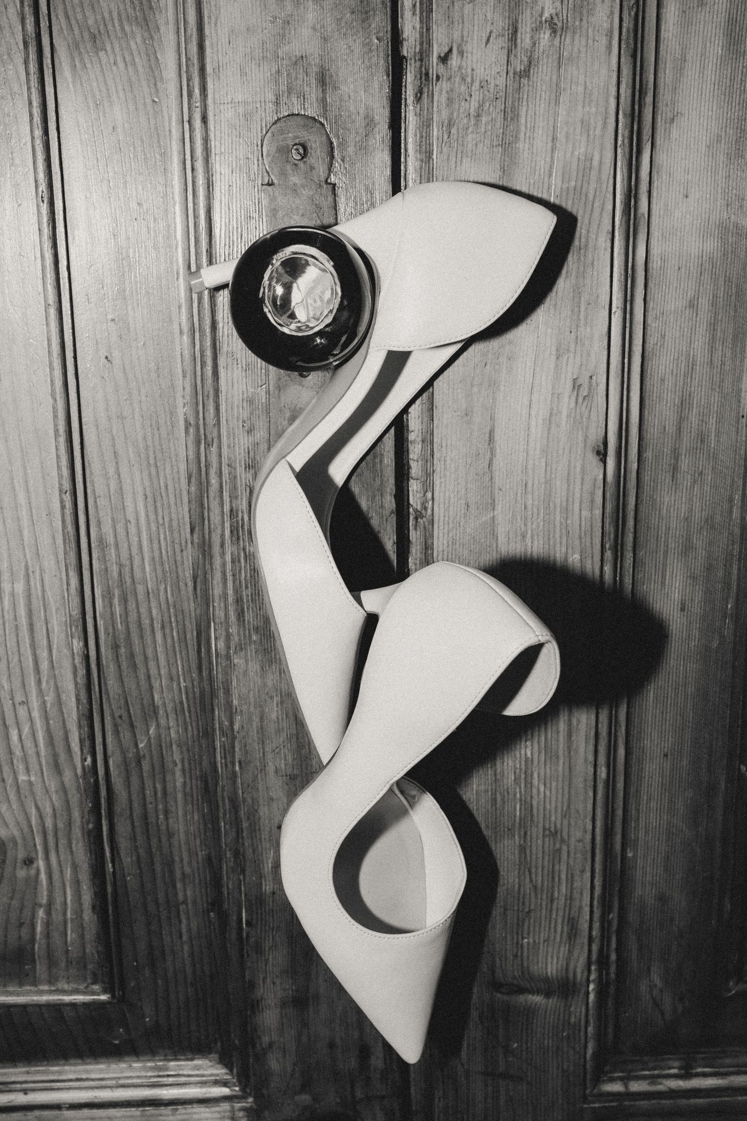 Black and white photo of white high heel shoes displayed against a wooden paneled wall.