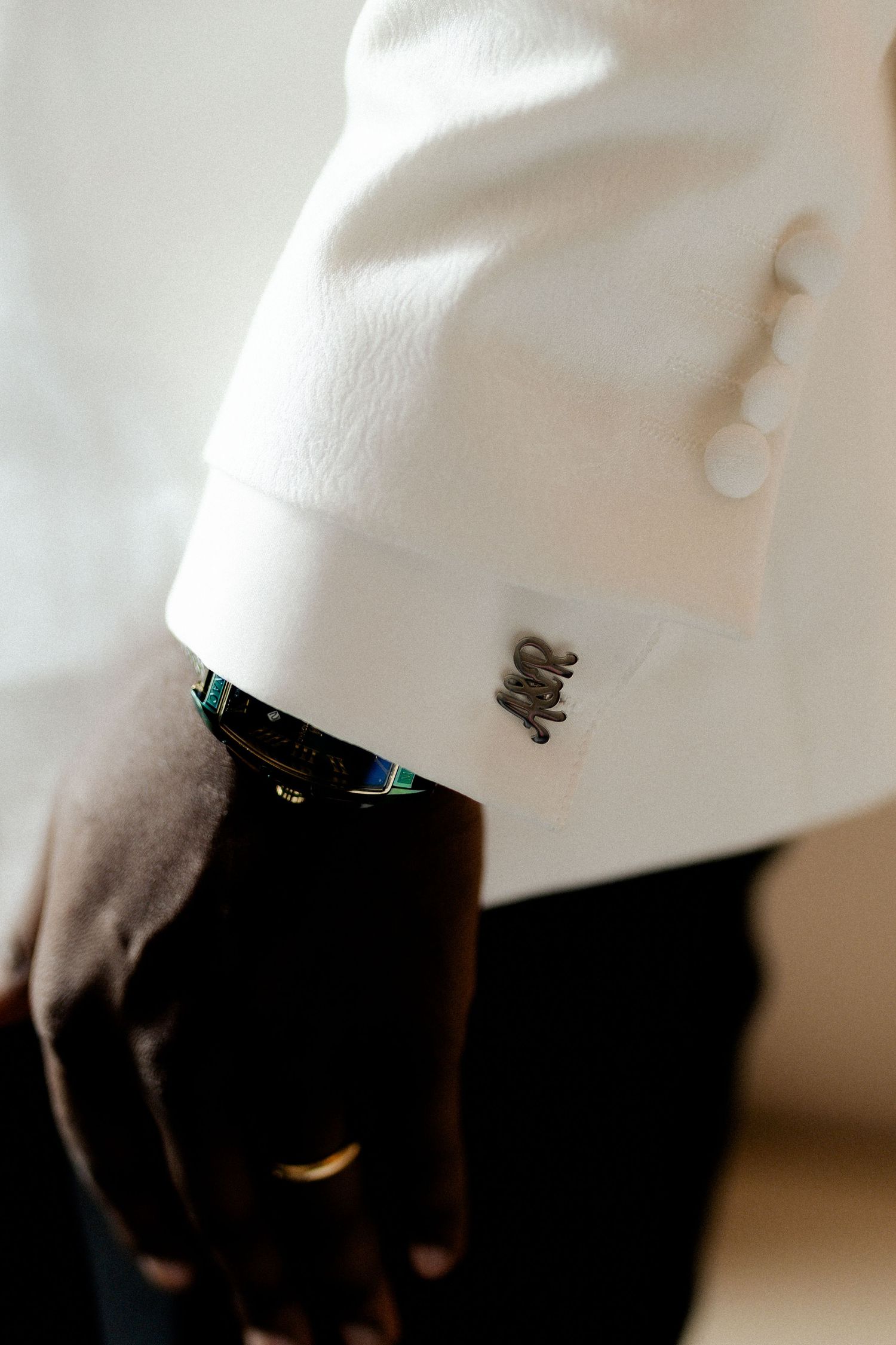 Close-up detail shot of a white tuxedo jacket sleeve with decorative cufflinks.