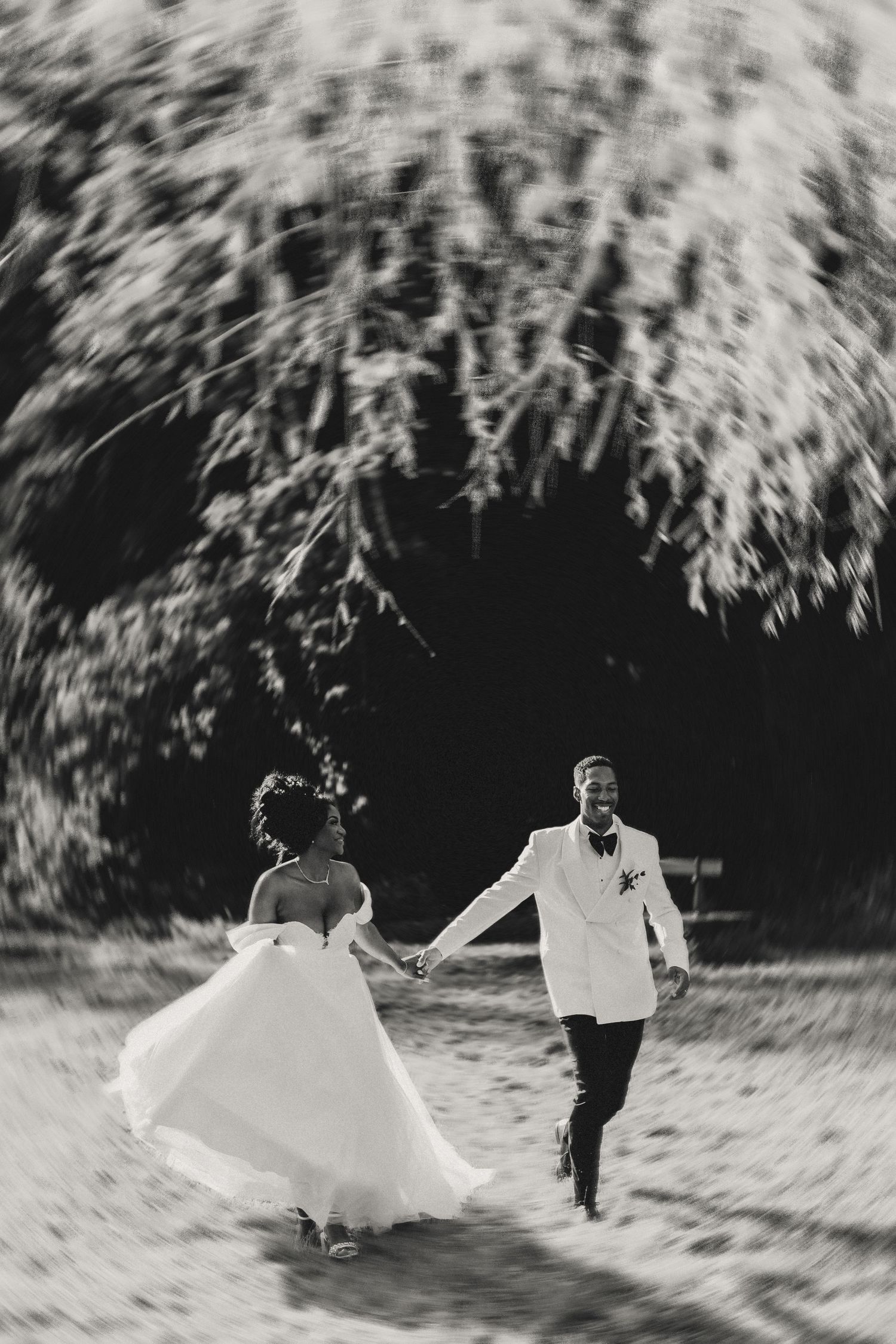 Black and white wedding photo showing couple running together outdoors, bride's dress flowing in motion.