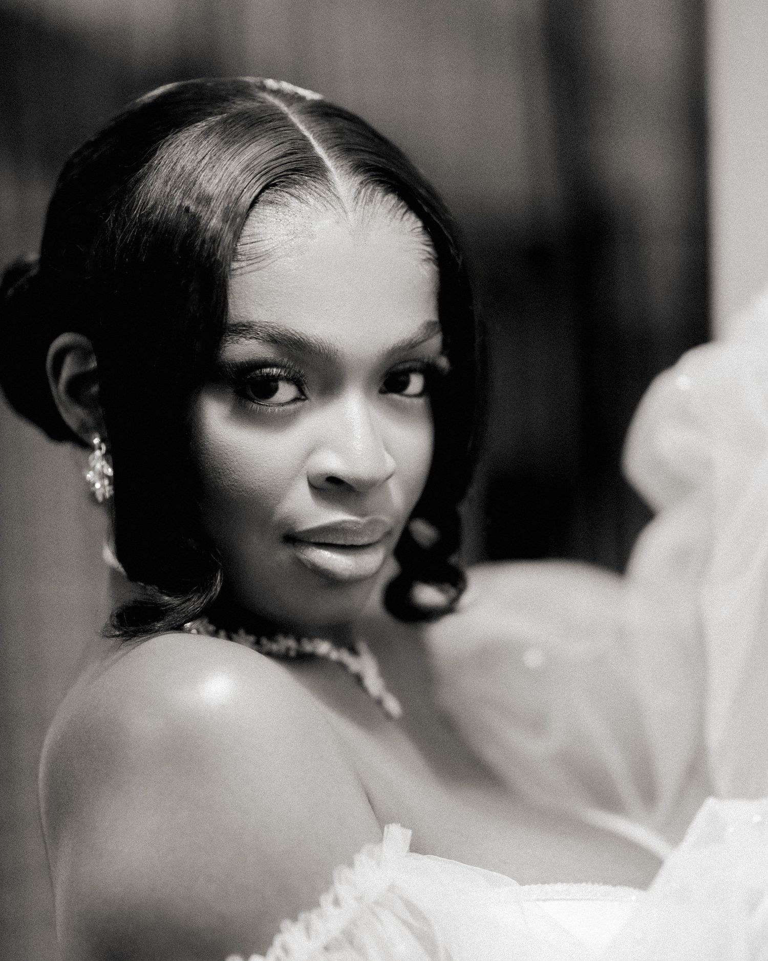 A portrait in black and white of someone wearing an elegant off-shoulder dress and jewelry.