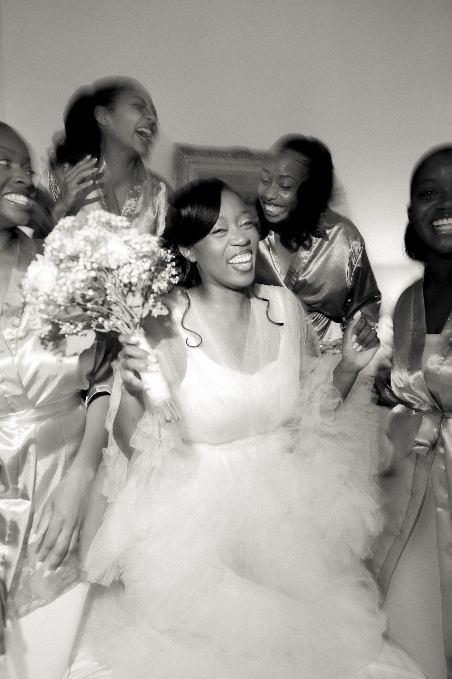 Candid black and white photo of bridesmaids laughing with the bride on her wedding day.