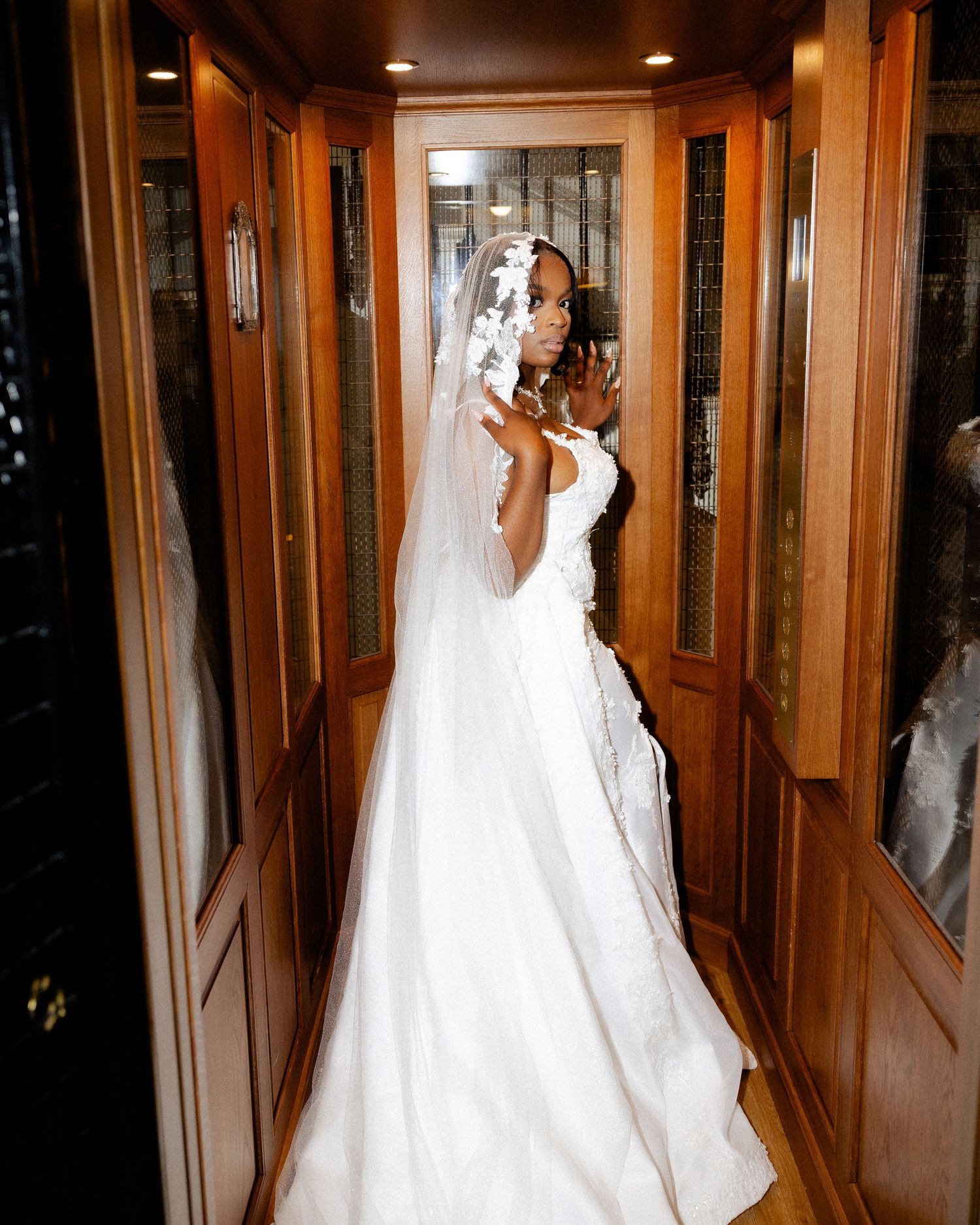 A bride in a classic white wedding gown and veil poses in an elegant wood-paneled hallway.