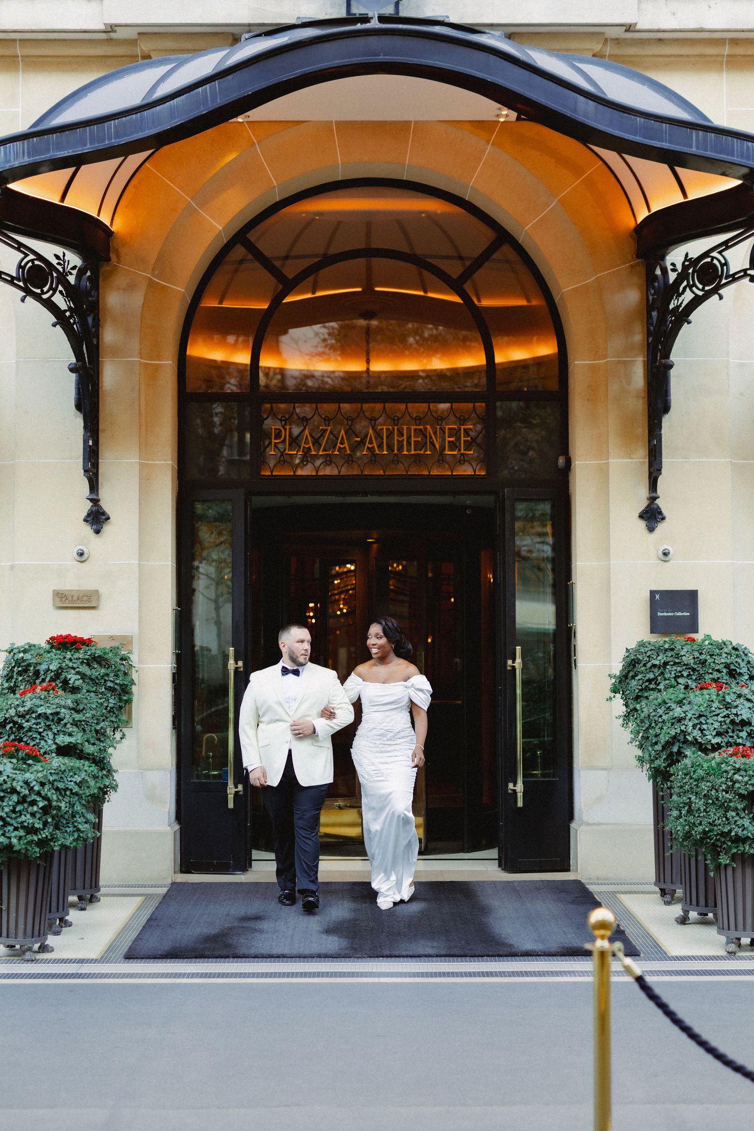 Elegant entrance of Plaza Athenee hotel in Paris with ornate archway and manicured topiaries flanking the doorway.