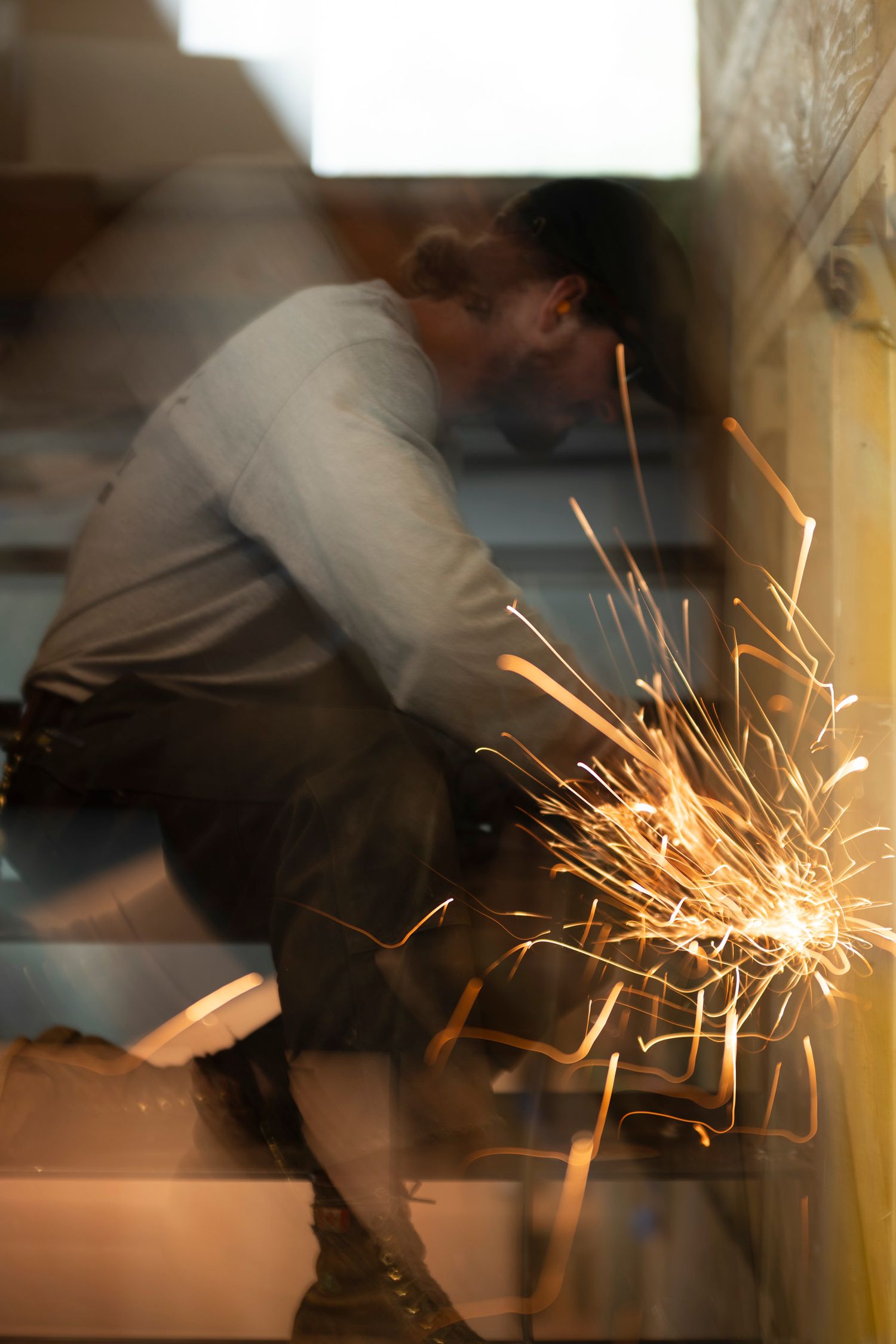 Worker grinding metal with bright orange sparks flying in a dimly lit construction environment.